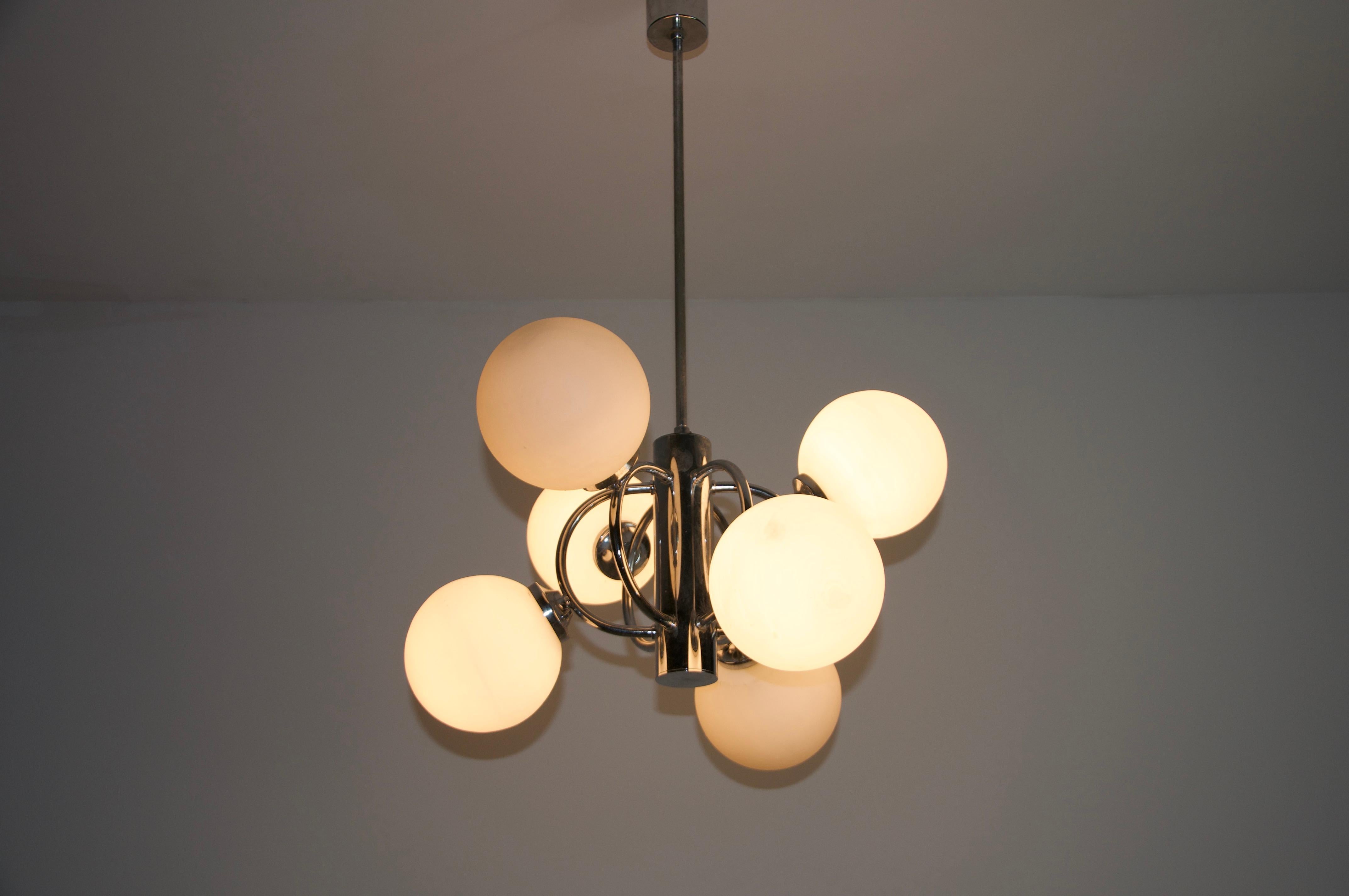 This midcentury chandelier by Kaiser Leuchten, crafted in Germany in the 1960s, showcases a captivating Space Age design. Its sleek, futuristic aesthetic is highlighted by six beautifully rounded opaline glass balls that provide a soft, diffused