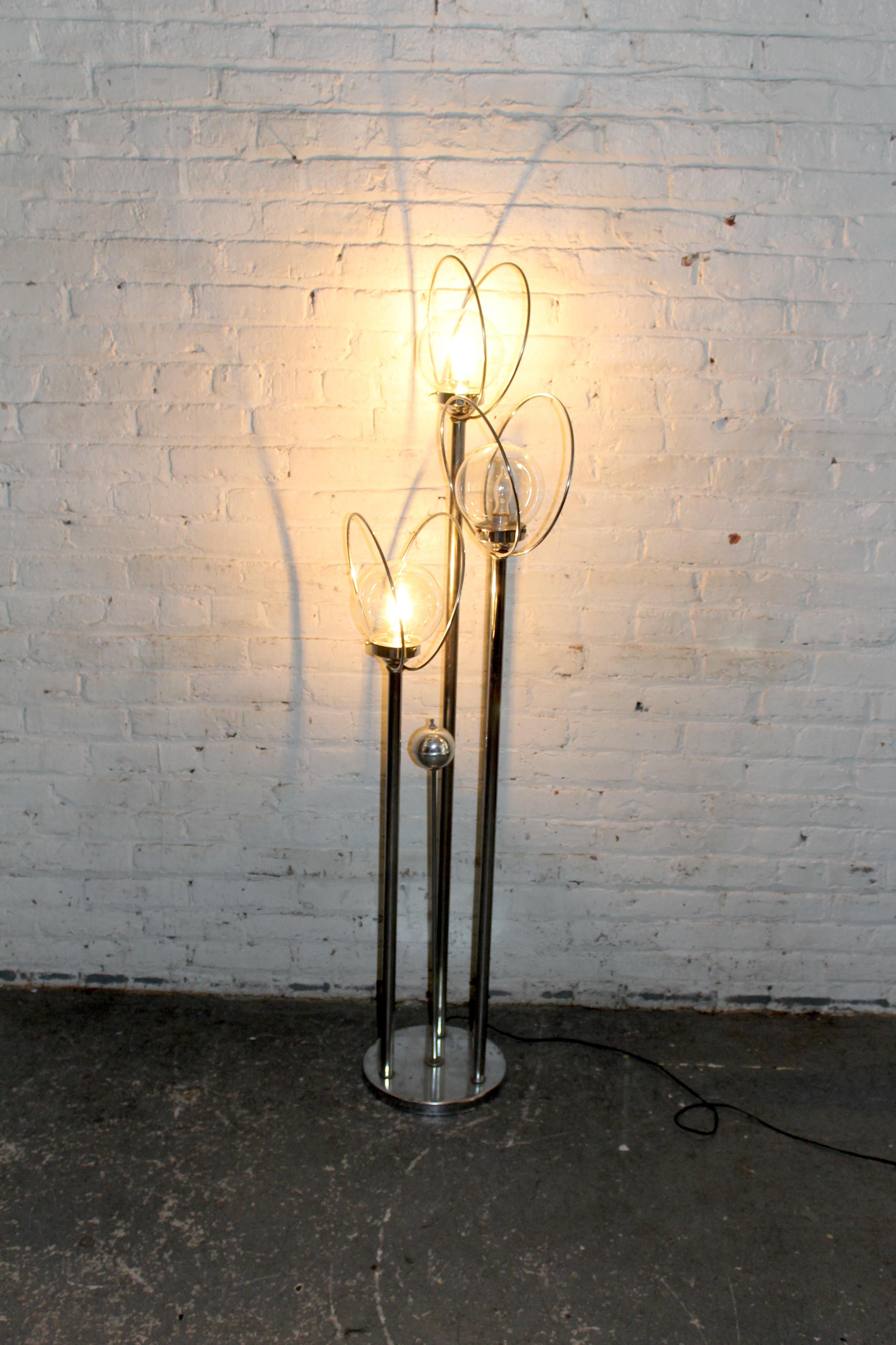 Striking floor lamp featuring a futuristic chrome design with three globe lights encased in sculptural elliptical wire frames. Each clear glass orb houses a single bulb, supported by sleek chrome poles of varying height for a dynamic, space-age