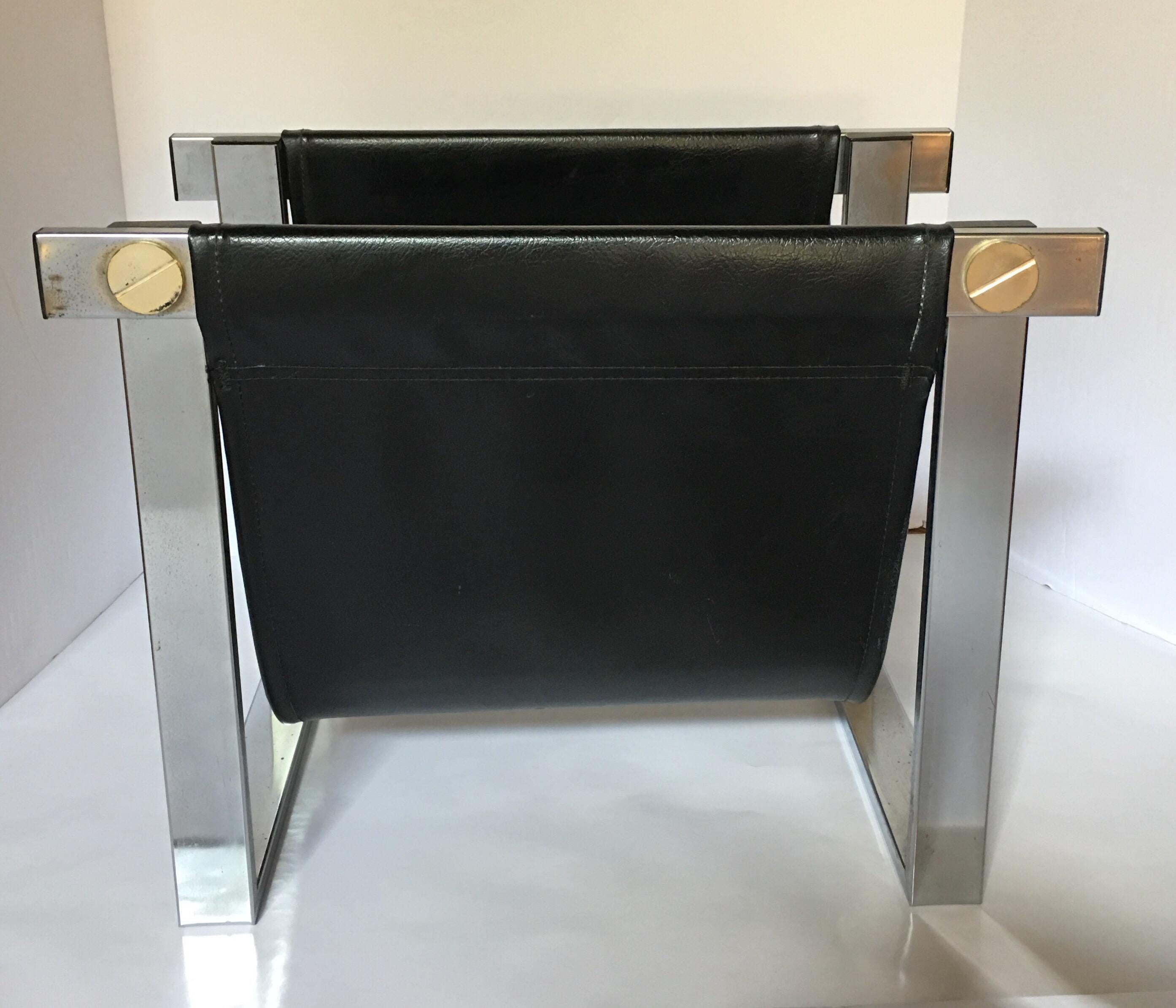 Mid-Century Modern magazine rack holder featuring a polished chrome frame with a faux black leather sling and oversized decorative gold tone hardware/screws. In the style of William Plunkett.