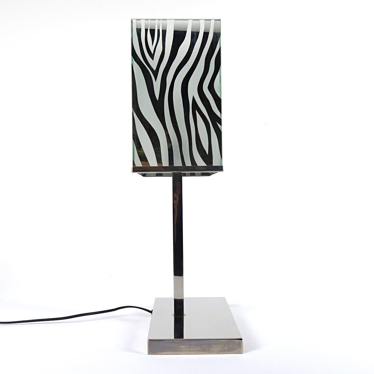 Stylish table lamp with a chrome base and mirror glass shade with zebra print.
By the alternation of mirror glass and zebra print the light shine in a wonderful diffuse manner through the shade.
The base carries the light switch.
A tasteful