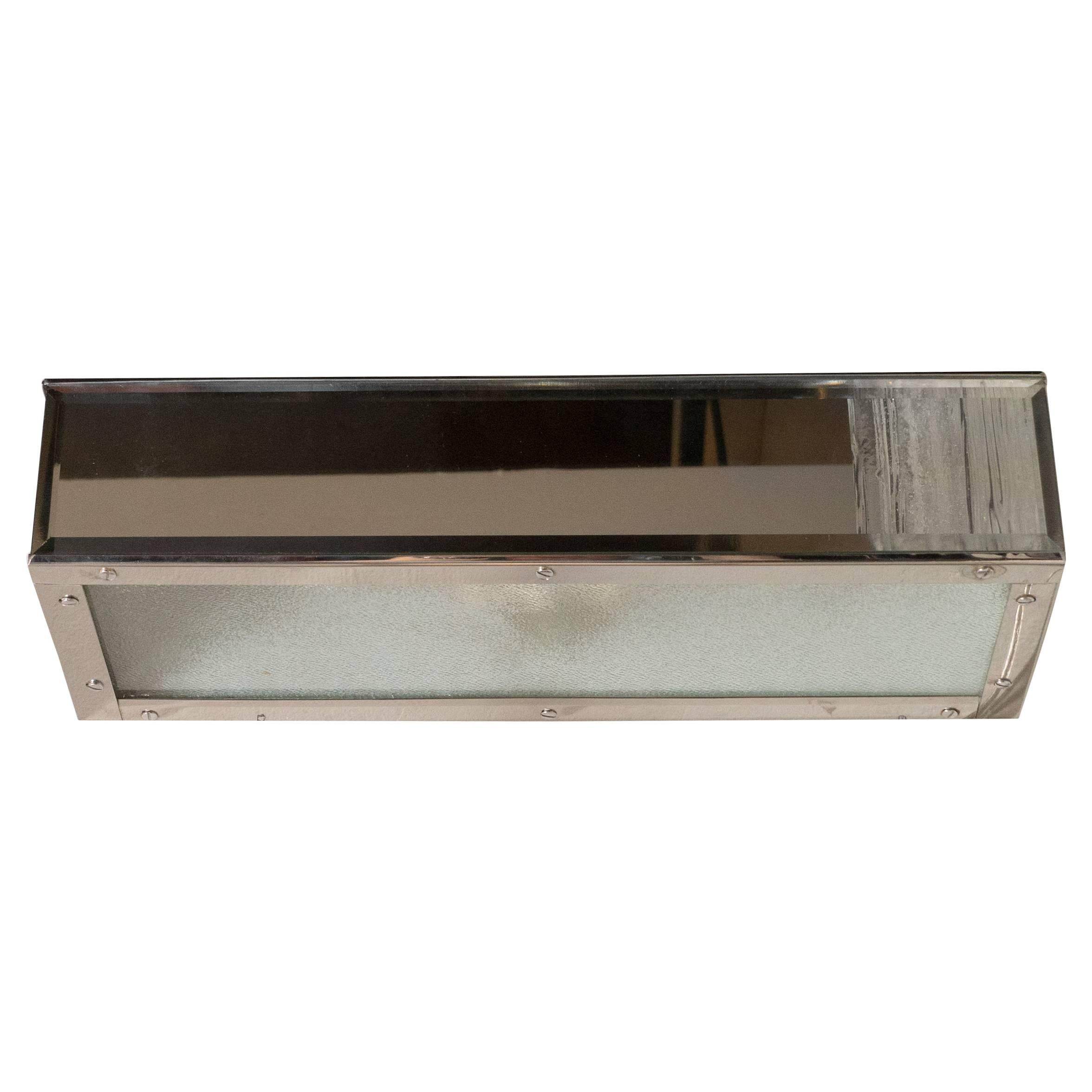 This elegant vanity light was realized in the United States, circa 1970. It features a rectangular chrome body with a bevelled mirror front. The bottom of the fixture is composed of textured glass with a subtle dappled texture. With its austere form