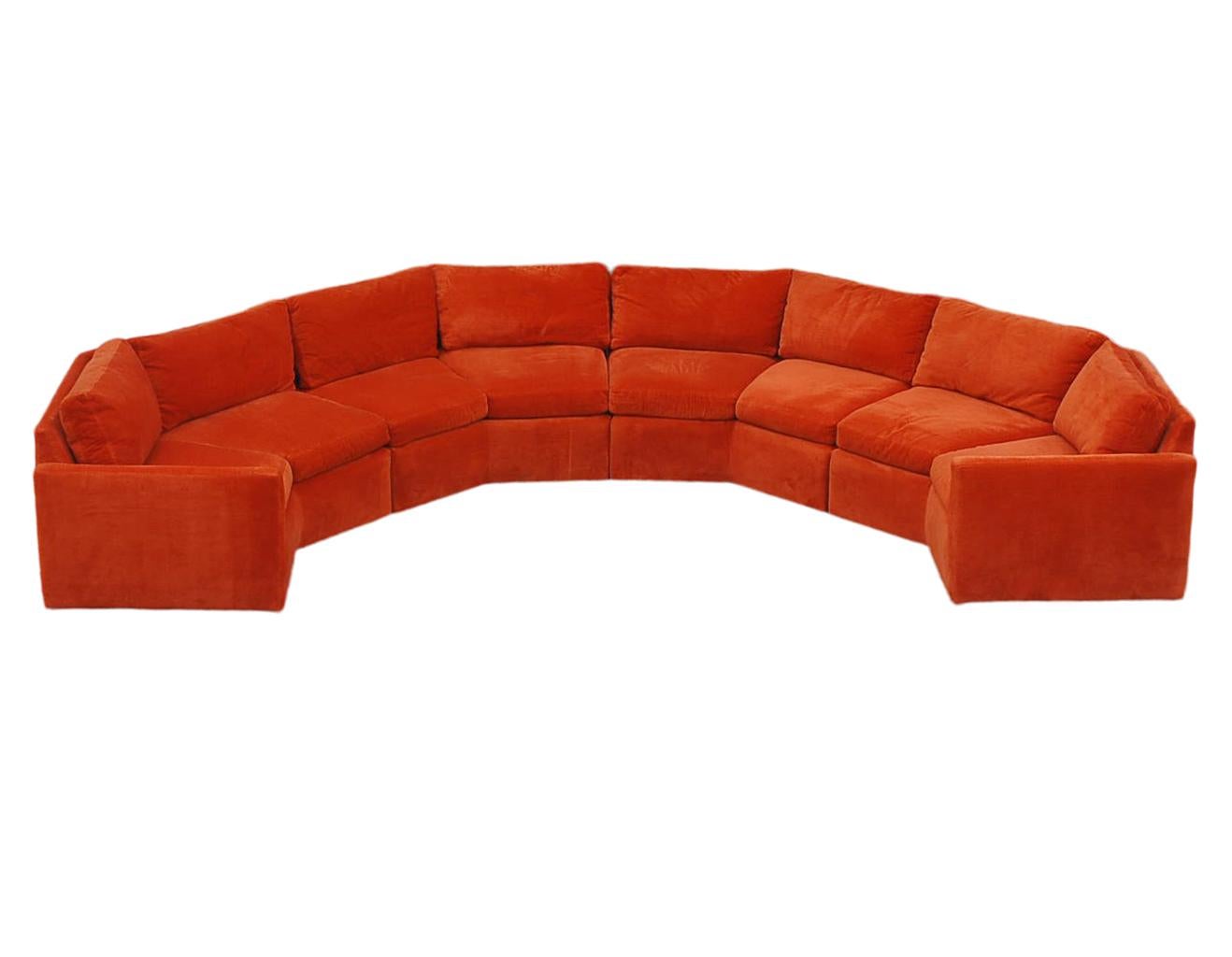 A large and impressive semi circular sofa designed by Milo Baugman and produced by Bernhardt in the 1970s. It features 4 angular sections retaining it's original orange velour upholstery. Reupholstery is recommended as there is a small tear in one
