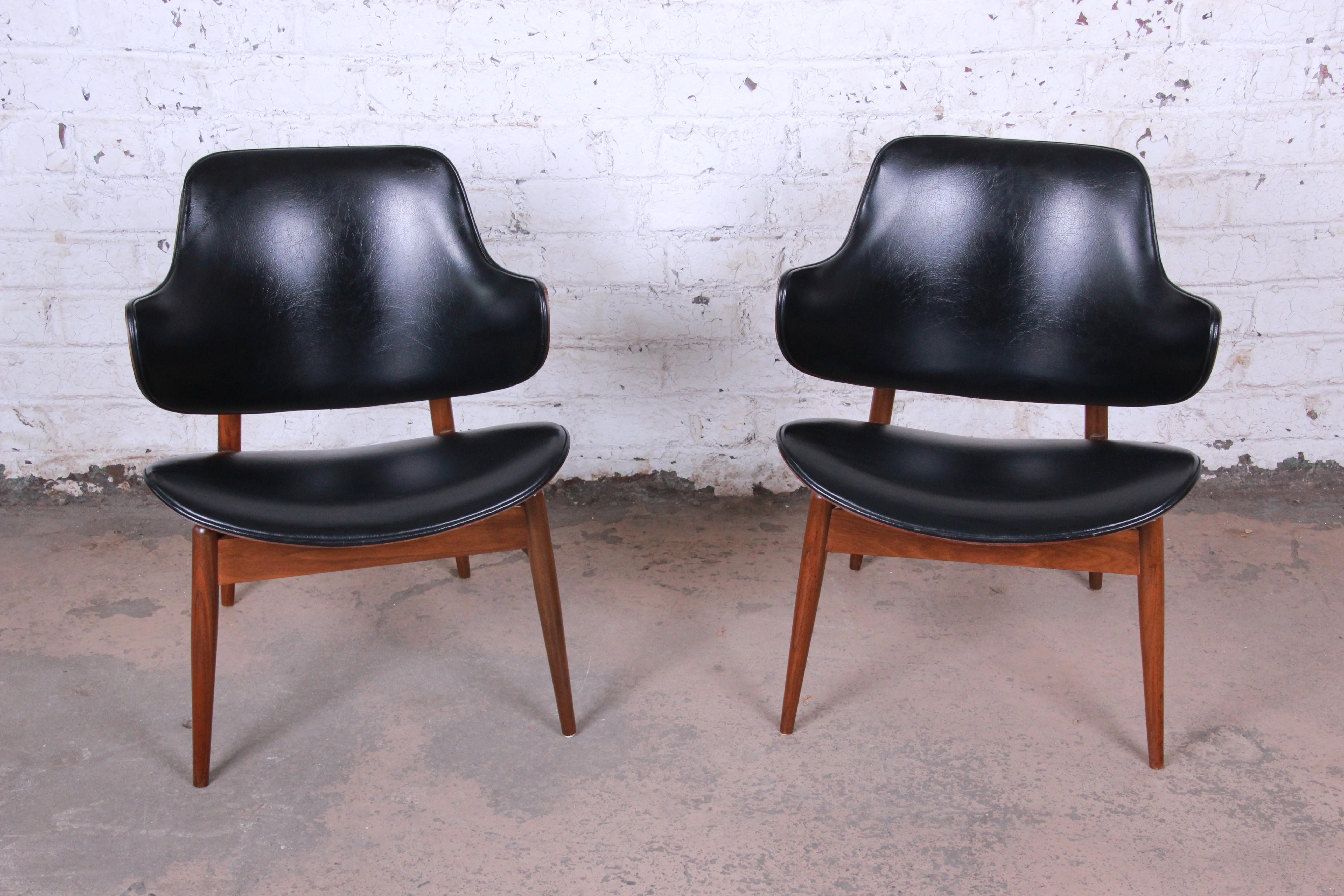 An exceptional pair of Mid-Century Modern club chairs designed by Seymour James Wiener for Kodawood. The chairs feature a stylish sculptural design, with clam shell backs and seats. The walnut frames have gorgeous wood grain, and the original vinyl