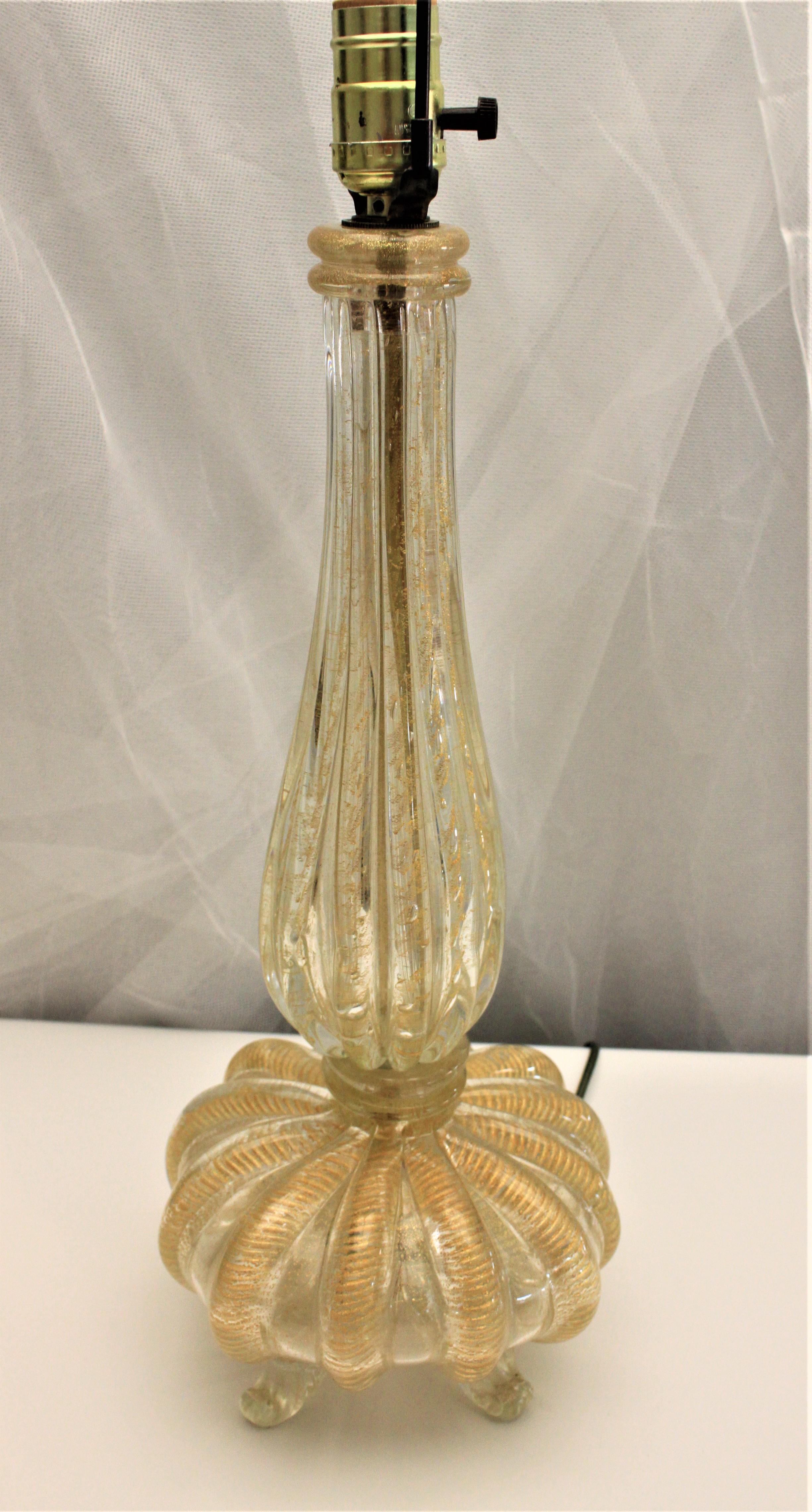 This Mid-Century Modern art glass table lamp is done with clear art glass with controlled bubbles and lots of gold flecks or aventurine with a tapered and ribbed body and a bulbous footed art glass base. Each rib of the lamp is accented by a gold