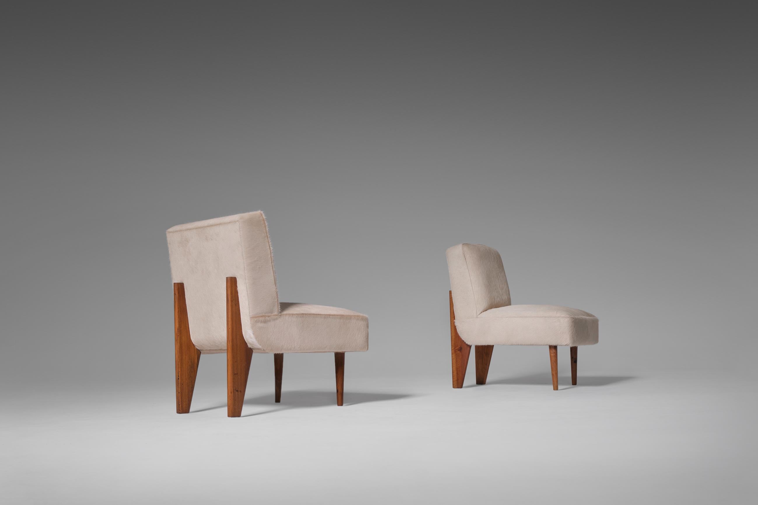 Striking pair of club chairs in the style of Jean Prouvé, early 1950's. Interesting modest yet striking design with nice Mid-Century Modern column shaped feet. The chairs are fully reconditioned and are upholstered in a neutral sand coloured pony