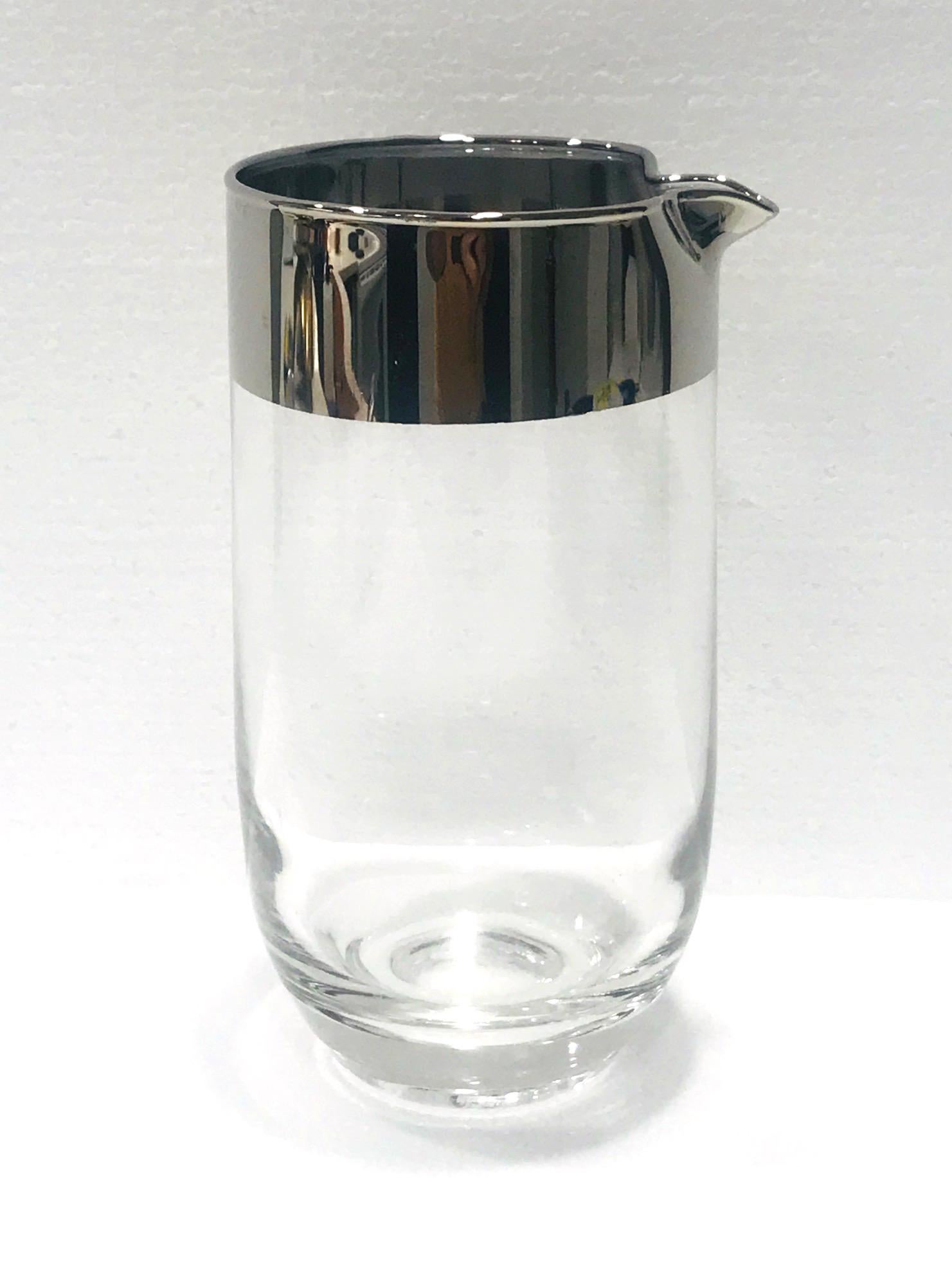 Mid-Century Modern cocktail shaker or carafe by Dorothy Thorpe, known for her iconic barware designs, circa 1960. The glass cocktail mixer has a minimalist design featuring a striking silver overlay rim and a tapered base.
The pitcher has a