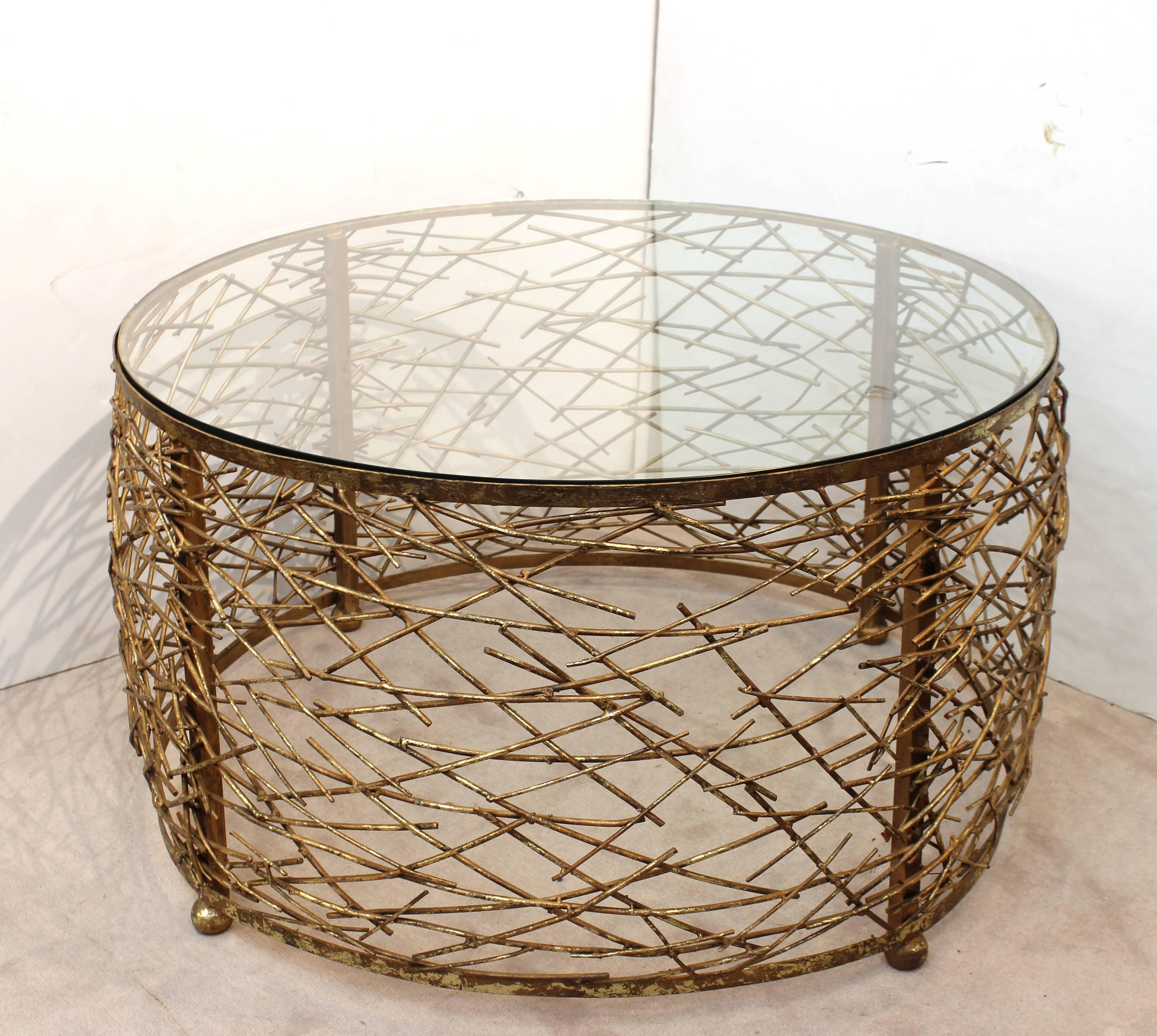 Mid-Century Modern cocktail table with round glass top and metal base. The base is nest shaped with numerous overlapping metal 'twigs.' Crafted in metal with gold colored finish. The table stands on several spherical feet. Wear to metal and finish
