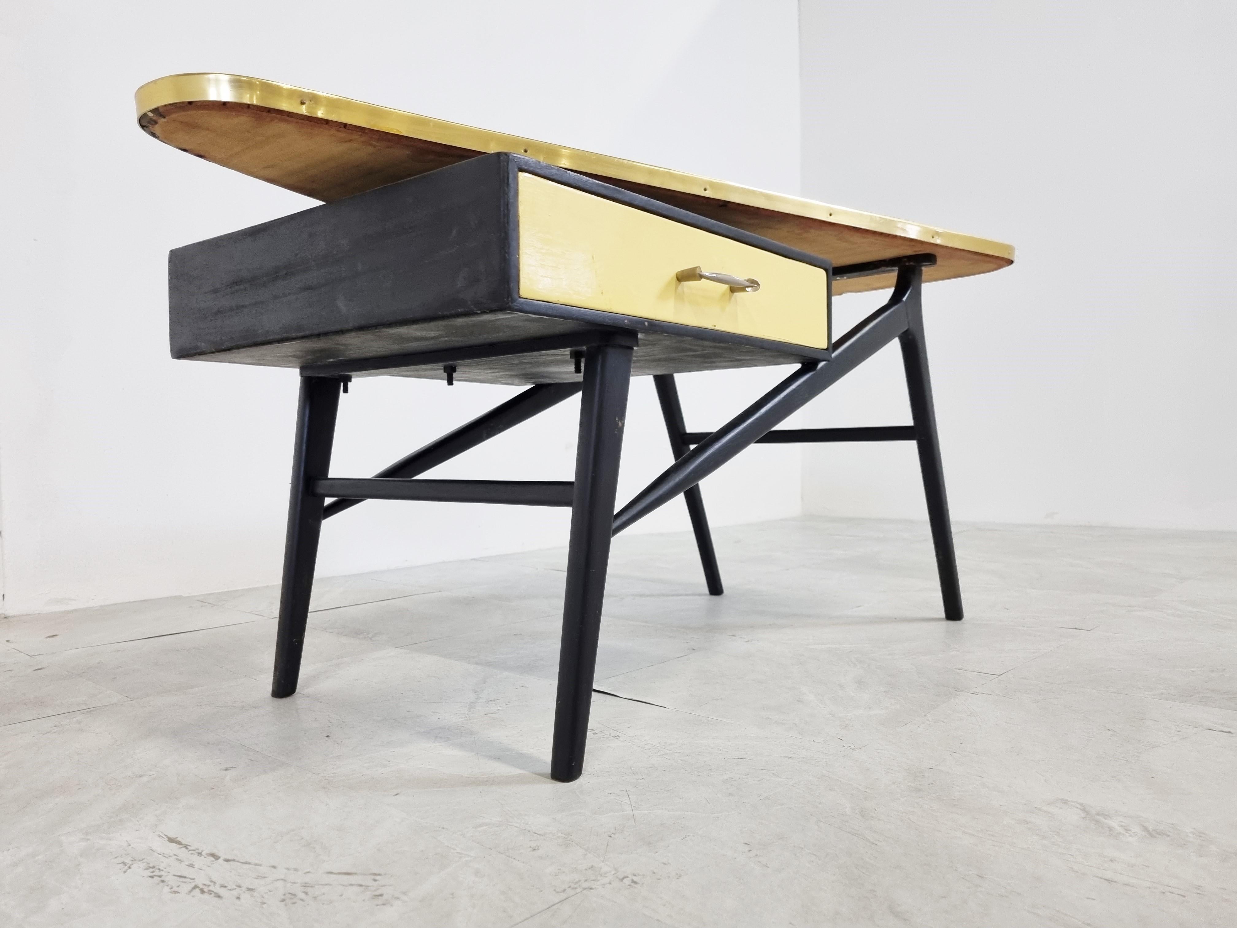 Mid-Century Modern coffee table with a triangular yellow wooden top, elegantly designed black lacquered wooden base and a drawer.

Beautiful design from the 50's, with a nicely shaped handle on the drawer.

Good condition with normal age related