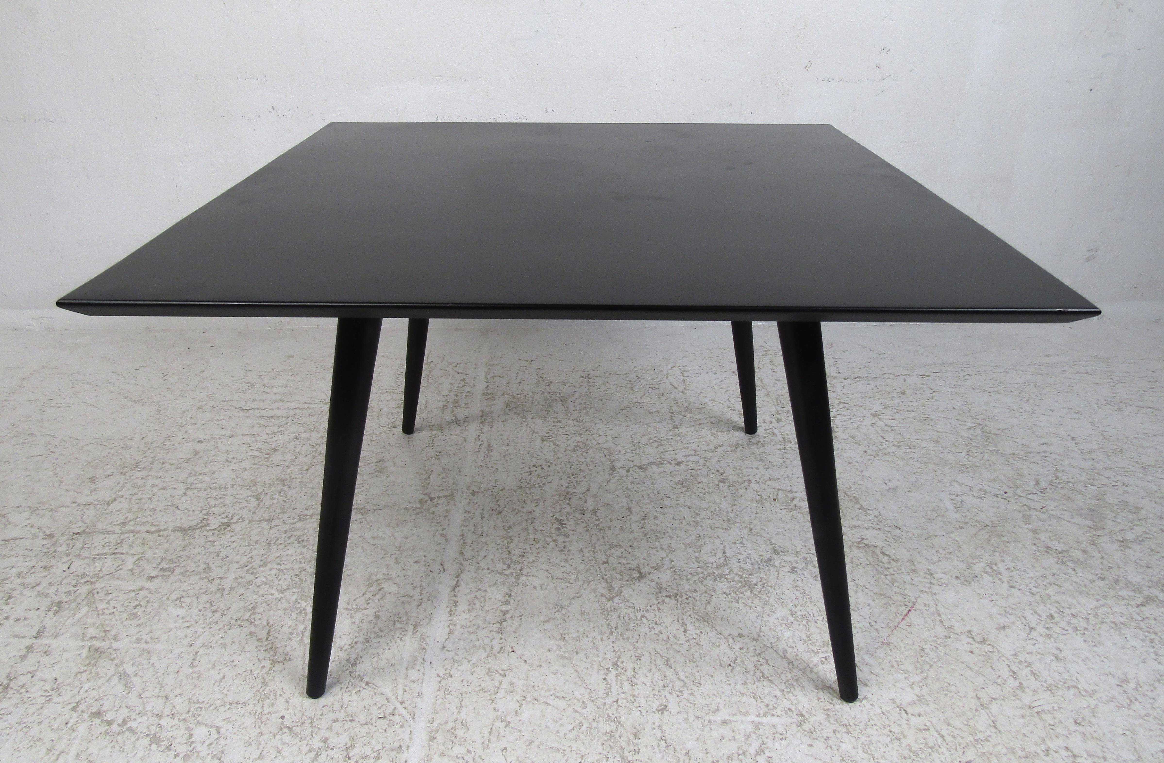 A beautiful vintage modern cocktail table by Paul McCobb with a black matte finish over wood and beveled edges. The iconic splayed and tapered legs add to the midcentury appeal. This sleek and functional square midcentury coffee table makes the