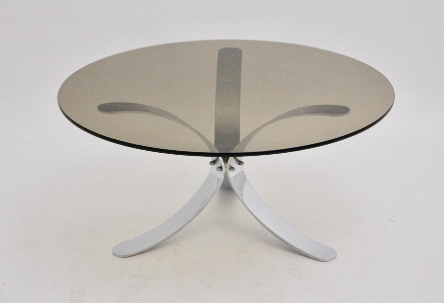 Cette table basse ou table de canapé présentée a été conçue et fabriquée vers 1970 en Allemagne.
La base à trois pieds en métal chromé présente une forme incurvée et est fixée au milieu par des vis chromées.
De plus, le plateau rond en verre fumé