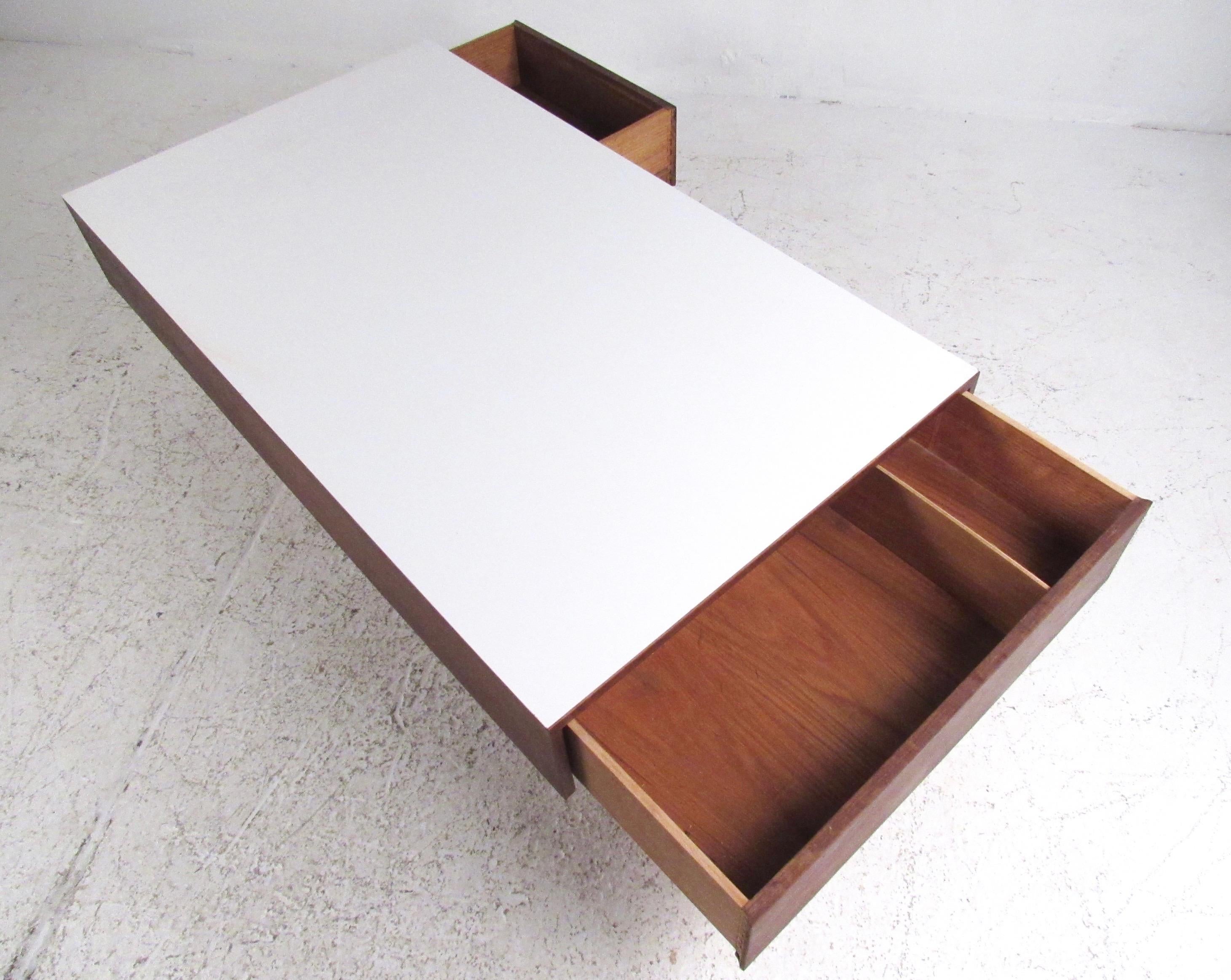 This large Mid-Century Modern walnut coffee table features tapered legs, two storage drawers, and a white formica top. The unique vintage appeal of this storage friendly coffee table adds retro charm as a center coffee table for home or business