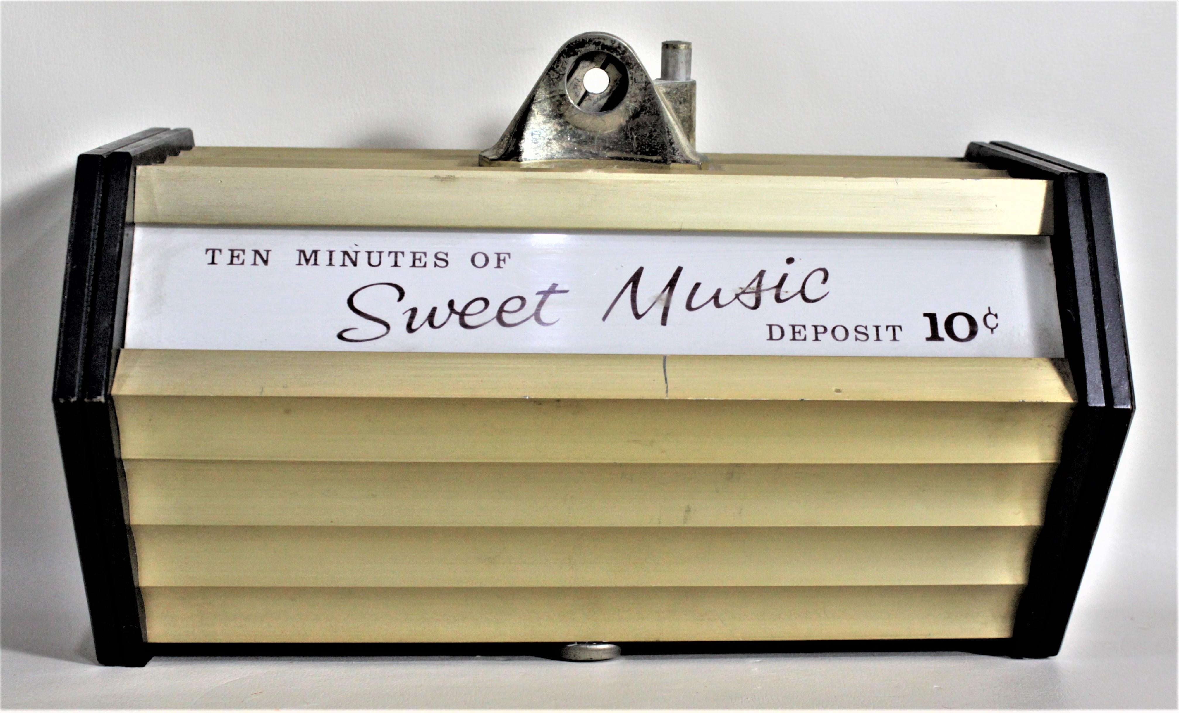 This coin operated commercial music box has no label or maker's mark on it, but it is presumed to have been made in the United States in approximately 1965 in the period Mid-Century Modern style. This wall mounted music box is done with gold tone