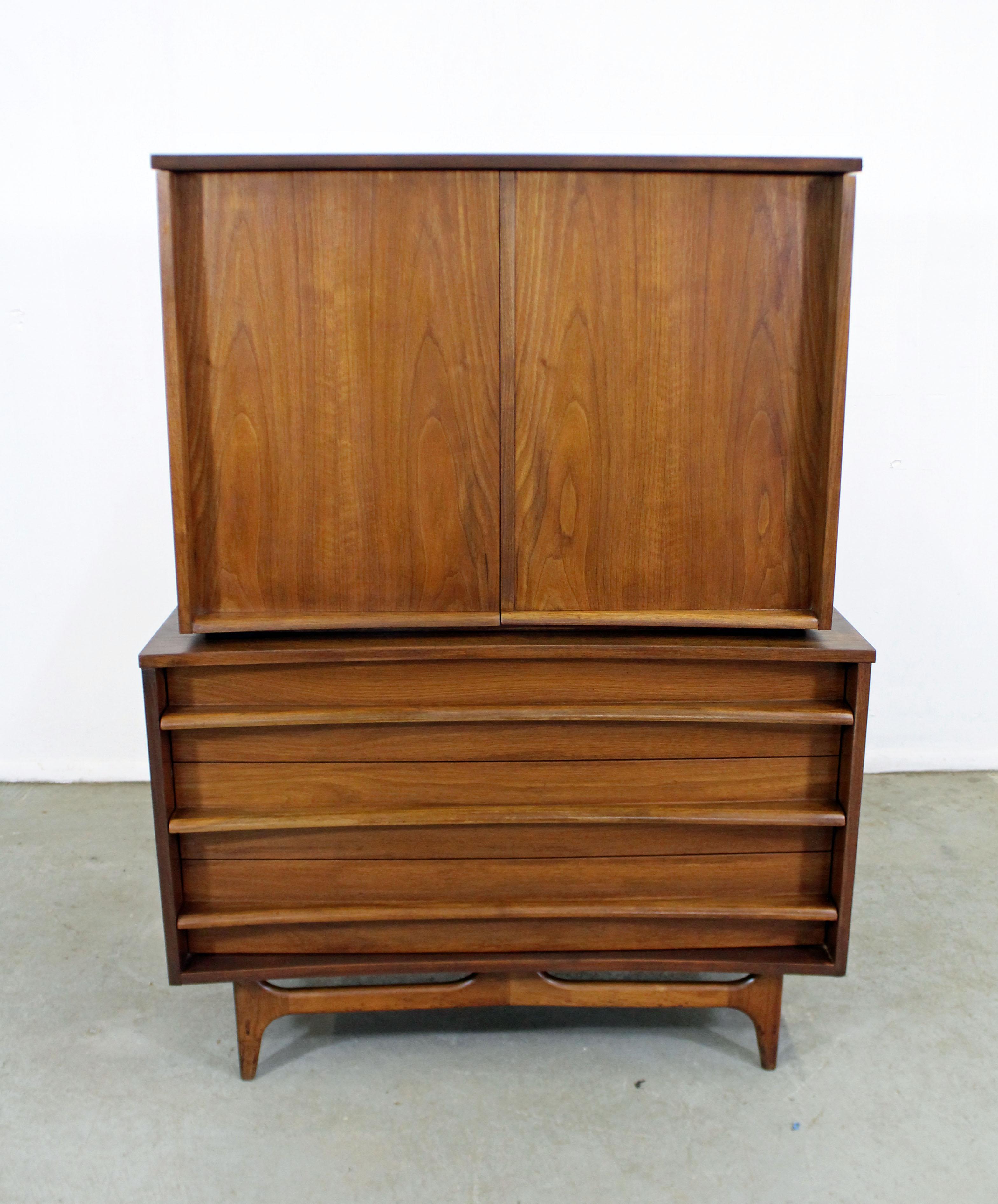 Offered is a beautiful Mid-Century Modern tall chest with ample storage space. This piece is made of walnut, featuring a concave front, 2 doors with six dovetailed drawers and inside shelving. It is in good vintage condition, shows slight age wear