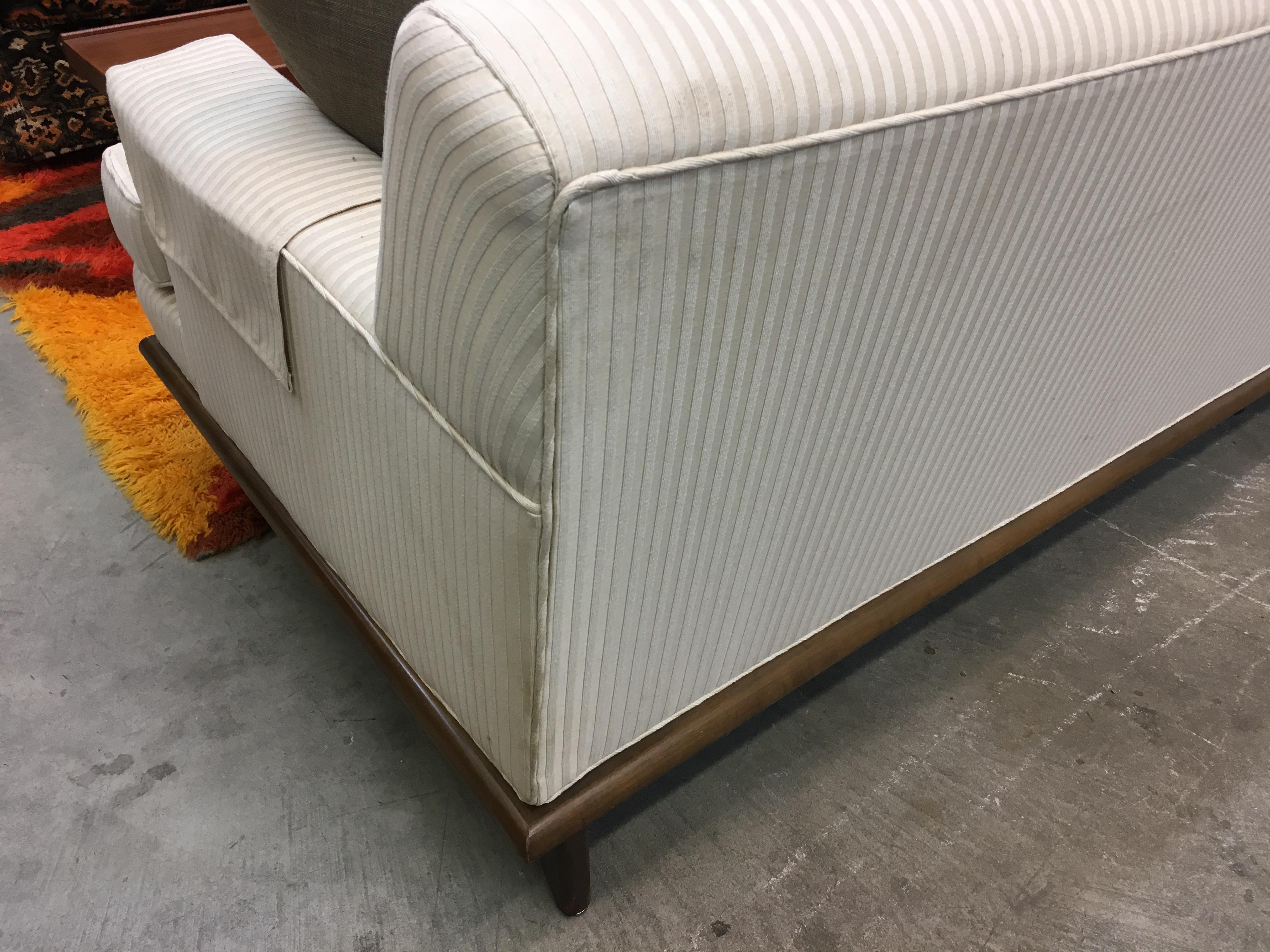 What a find. Offered is a Mid-Century Modern sofa with white textured upholstery on a wooden base. This sofa has a great modern look to it with a concave front. The sofa is in overall good condition, has small scratches on wood base and slight
