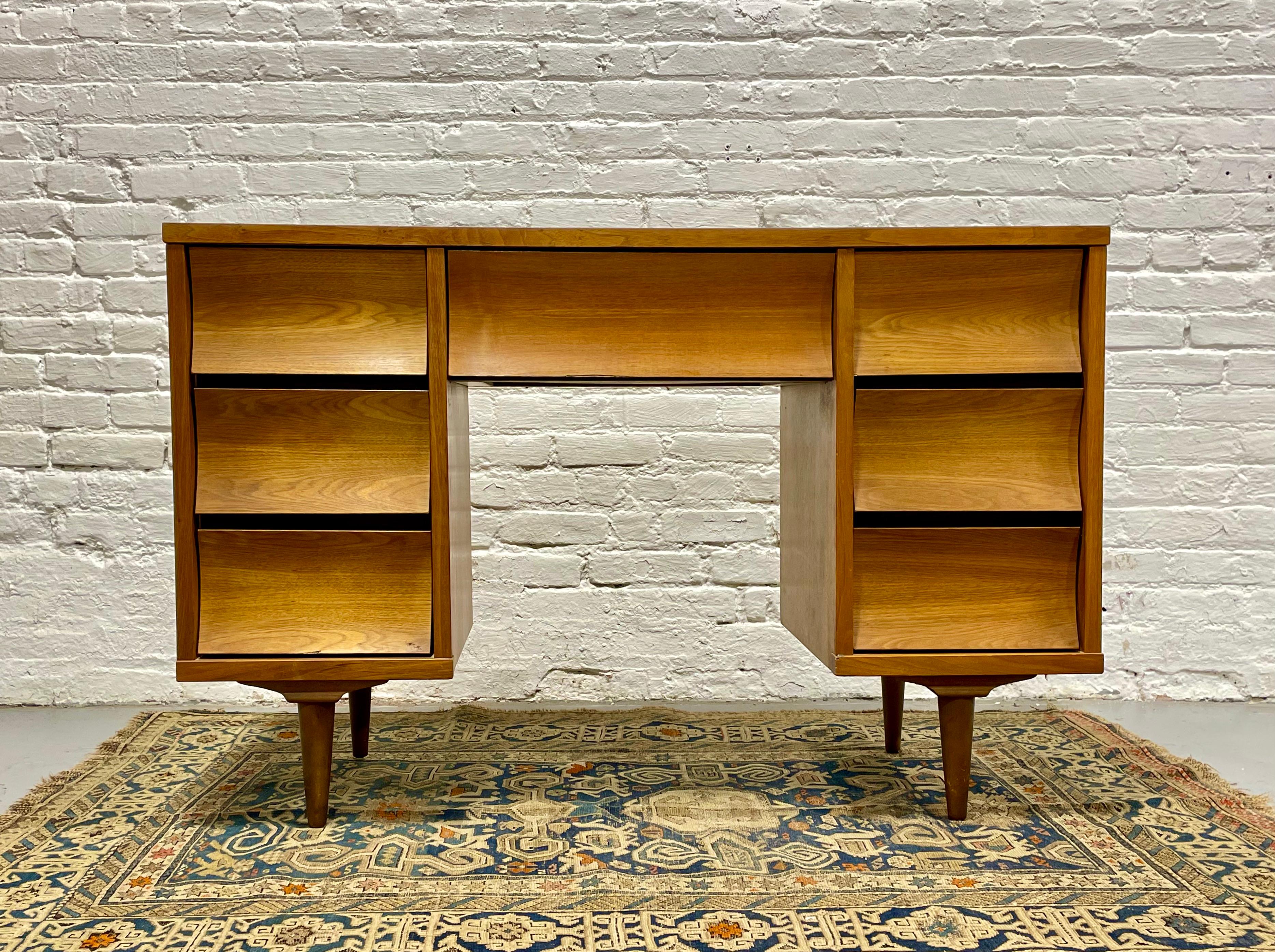 Mid Century Modern Walnut Desk by Johnson Carper, featuring concave drawers and seven deep and spacious drawers for plenty of storage space. The tabletop is a laminate (formica) woodgrain, perfect for withstanding the wear and tear of a work