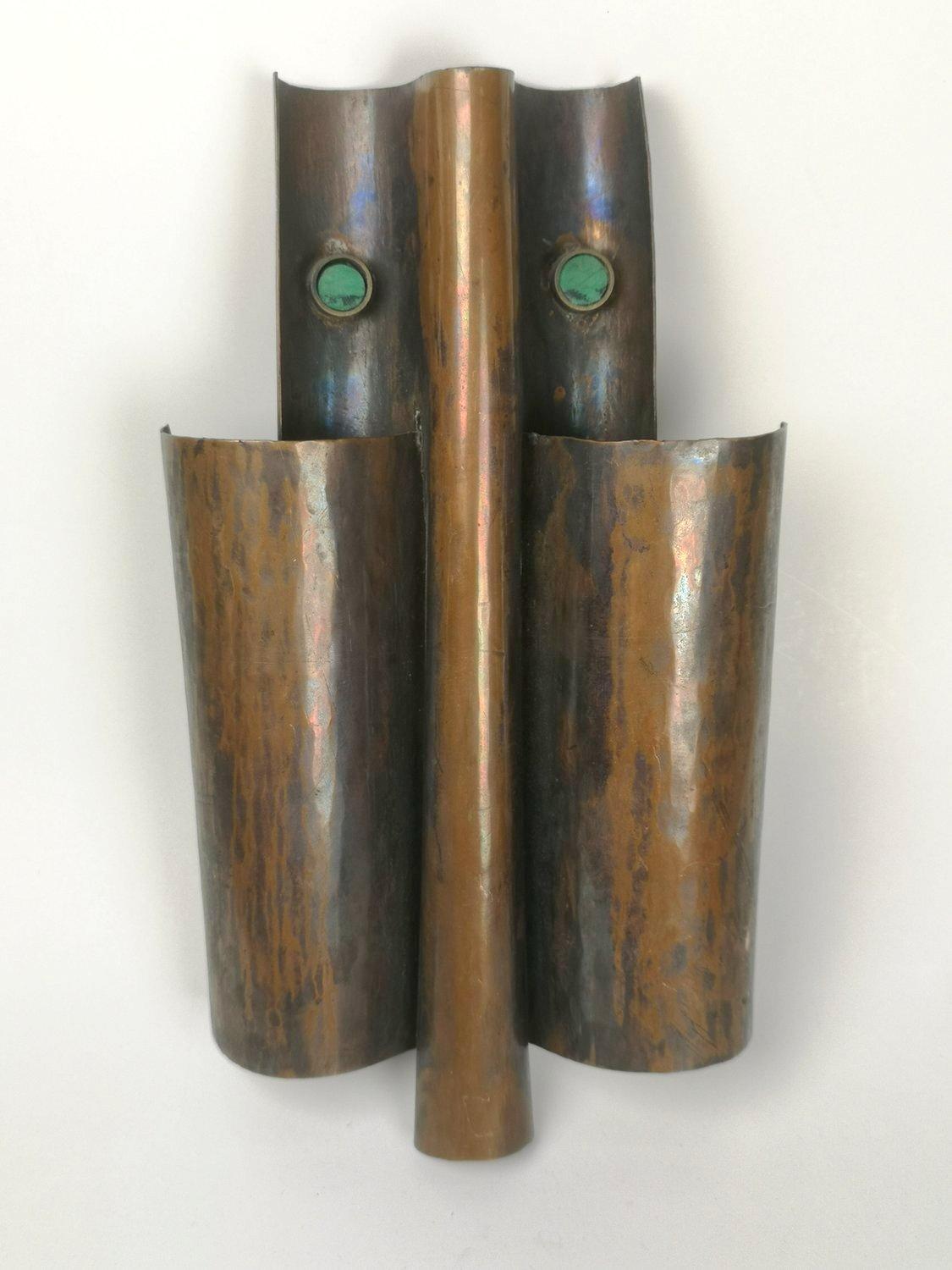 An applied art piece, made of copper depicting an abstract male head. The eyes are enameled. A very decorative item.