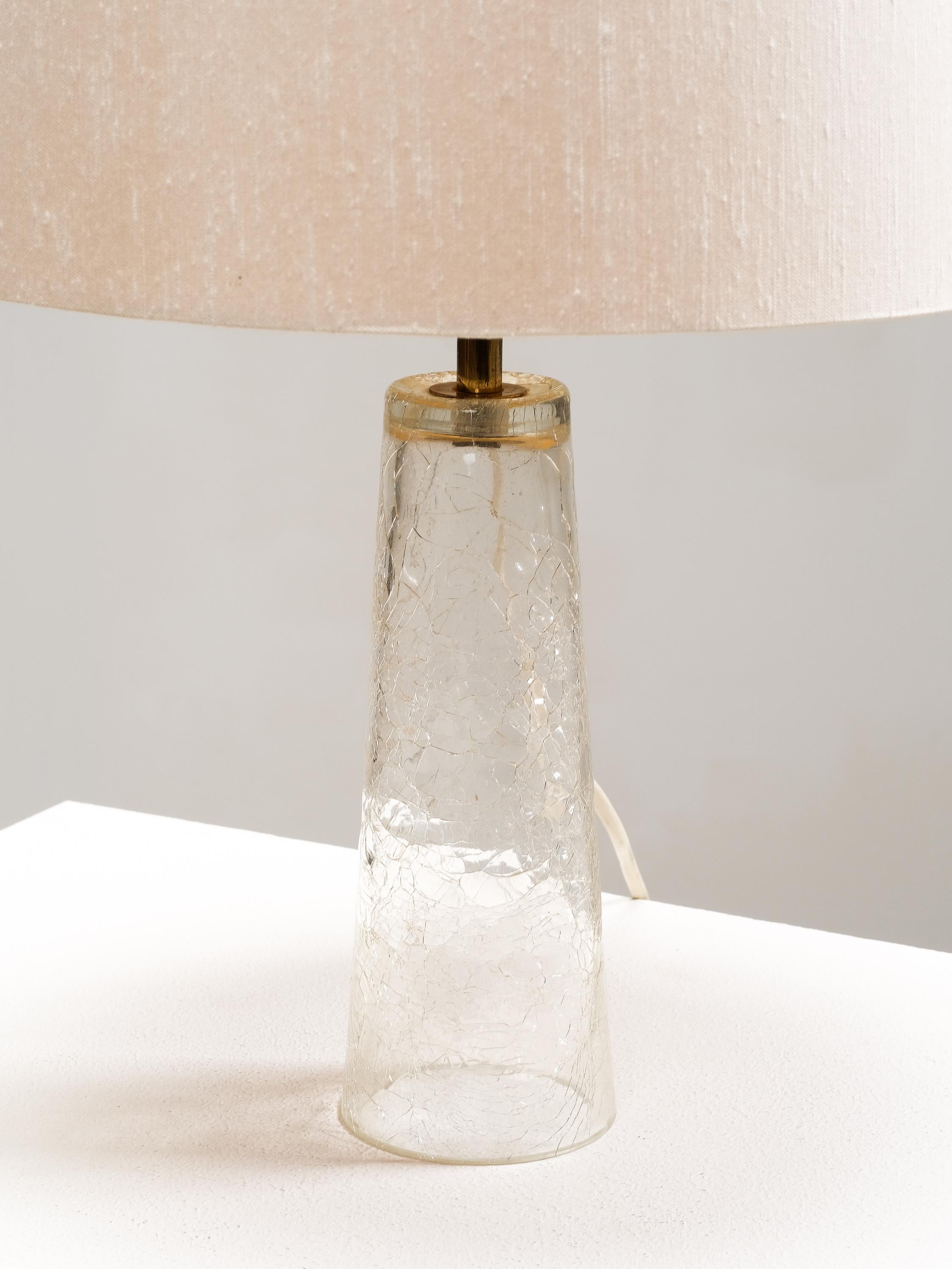 Impresionante ejemplo de diseño escandinavo, esta lámpara de sobremesa moderna de mediados de siglo fue producida por los estimados grandes almacenes finlandeses Stockmann en la década de 1960. La lámpara tiene una base de cristal craquelado de