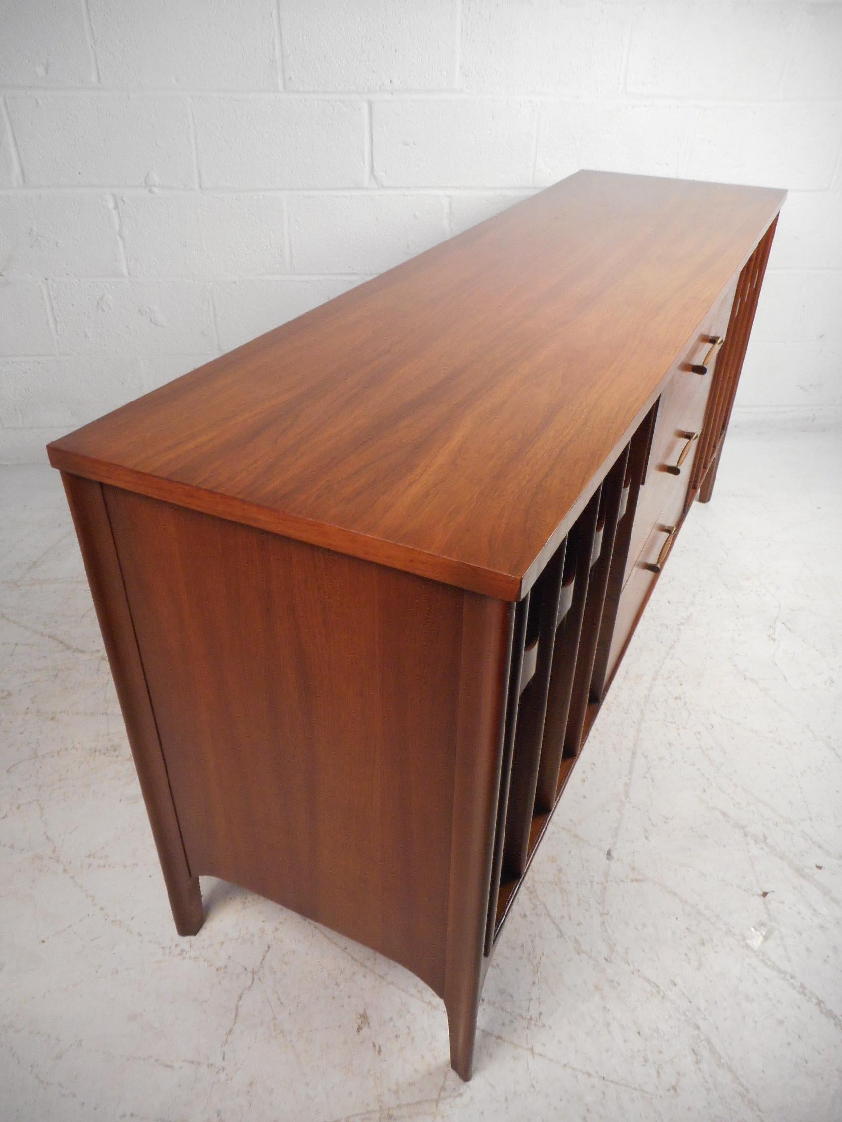 This unique Mid-Century Modern sideboard features walnut finish and a spacious mix of drawers and cabinets for efficient storage at home or office. Brasilia style sculptural door fronts add a unique modernist flair to this elegant storage credenza.