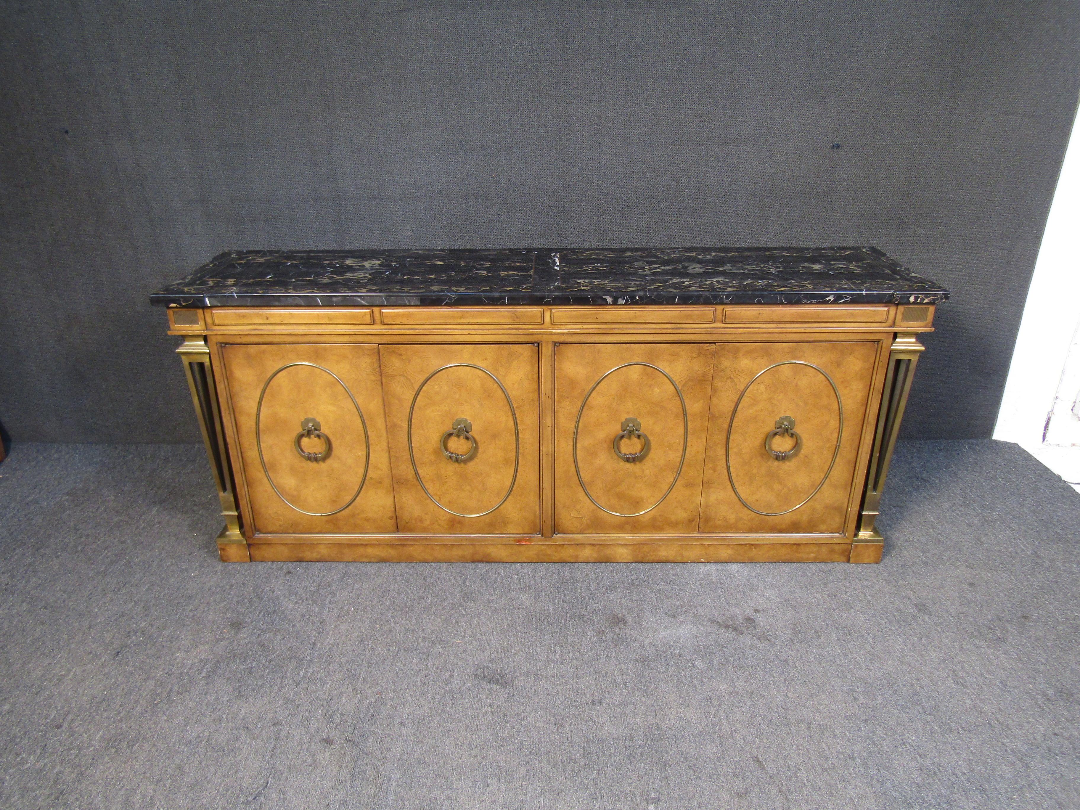 This vintage credenza by Mastercraft is an impressive piece of Mid-Century design. With radiant burl woodgrain, brass accents, a dark marble top, and elaborate details throughout, this credenza offers plenty of storage with a truly unique look.