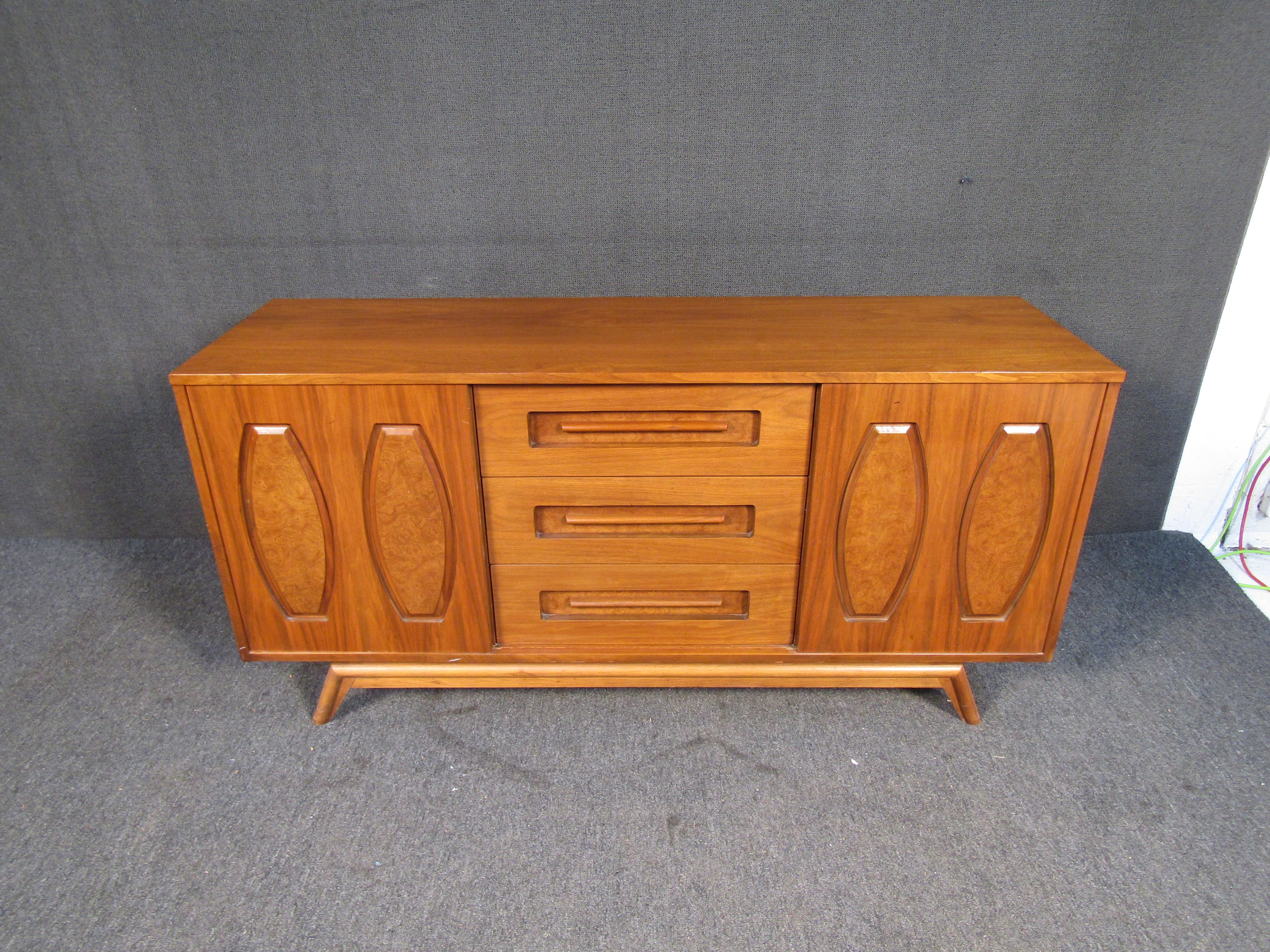 This large mid-century credenza is full of timeless style with its sculpted legs, decorated sliding doors, and beautiful warm wood grain. Please confirm item location with seller (NY/NJ).