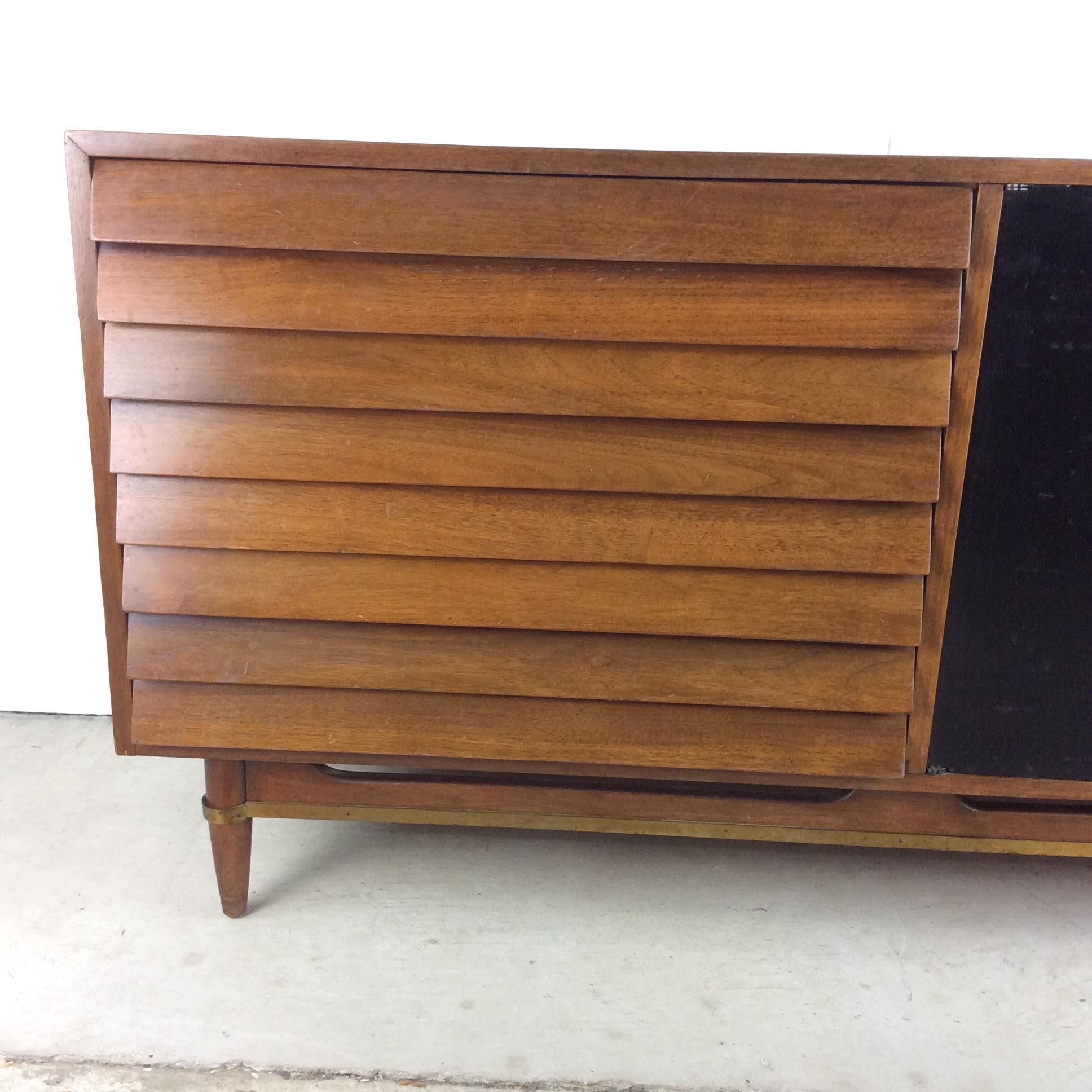 This Mid-Century Modern credenza from the Dania line by American of Martinsville features hardwood construction, walnut veneer with original finish, three large dovetailed drawers with louvered faces, black lacquered cabinet doors with three white