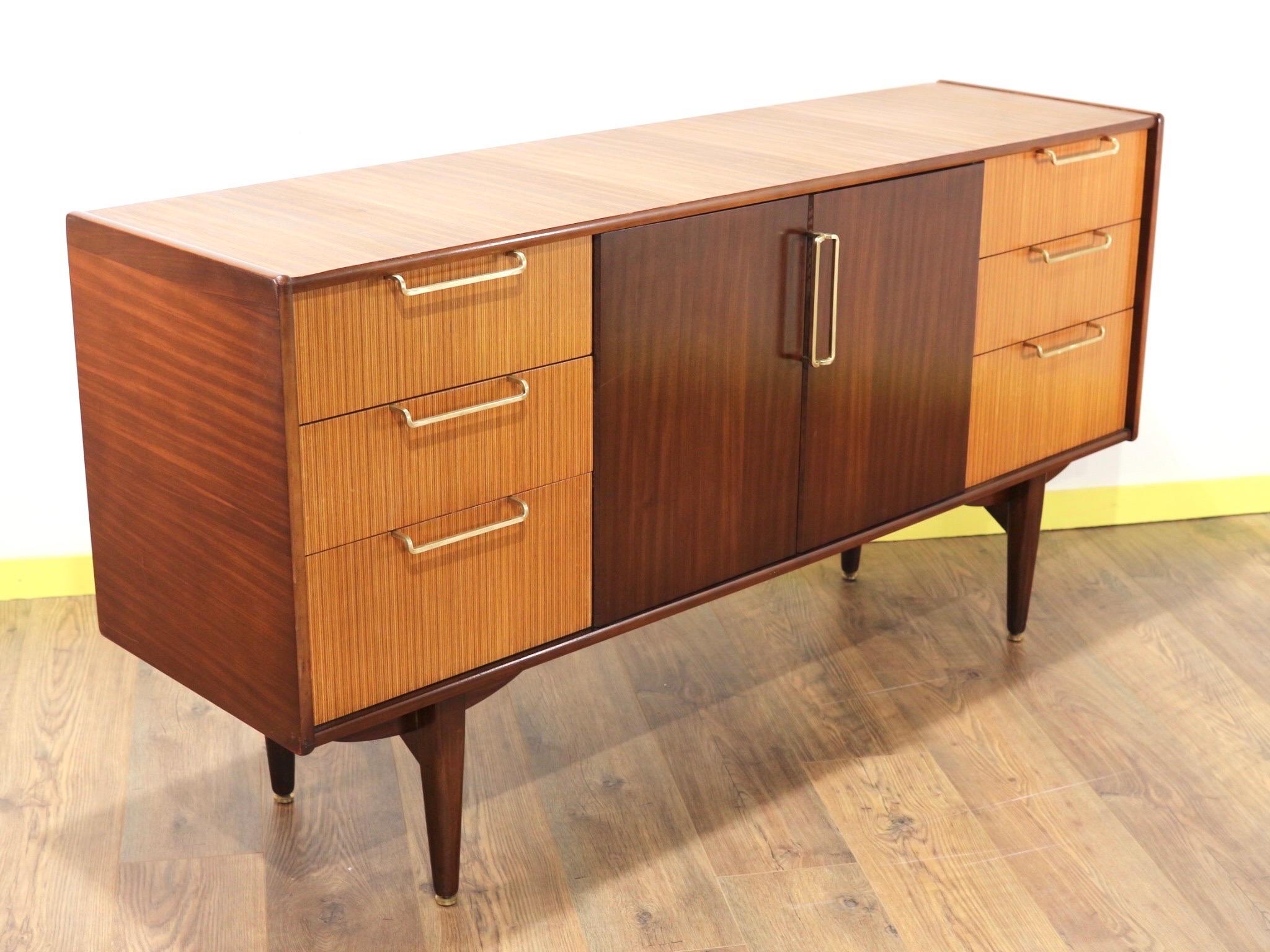 Mid-century credenza produced in England during the 1960s by Beutility.
This walnut credenza has central cabinet space which is flanked by three ash drawers with brass pulls either side. The credenza itself is walnut and stands on its original