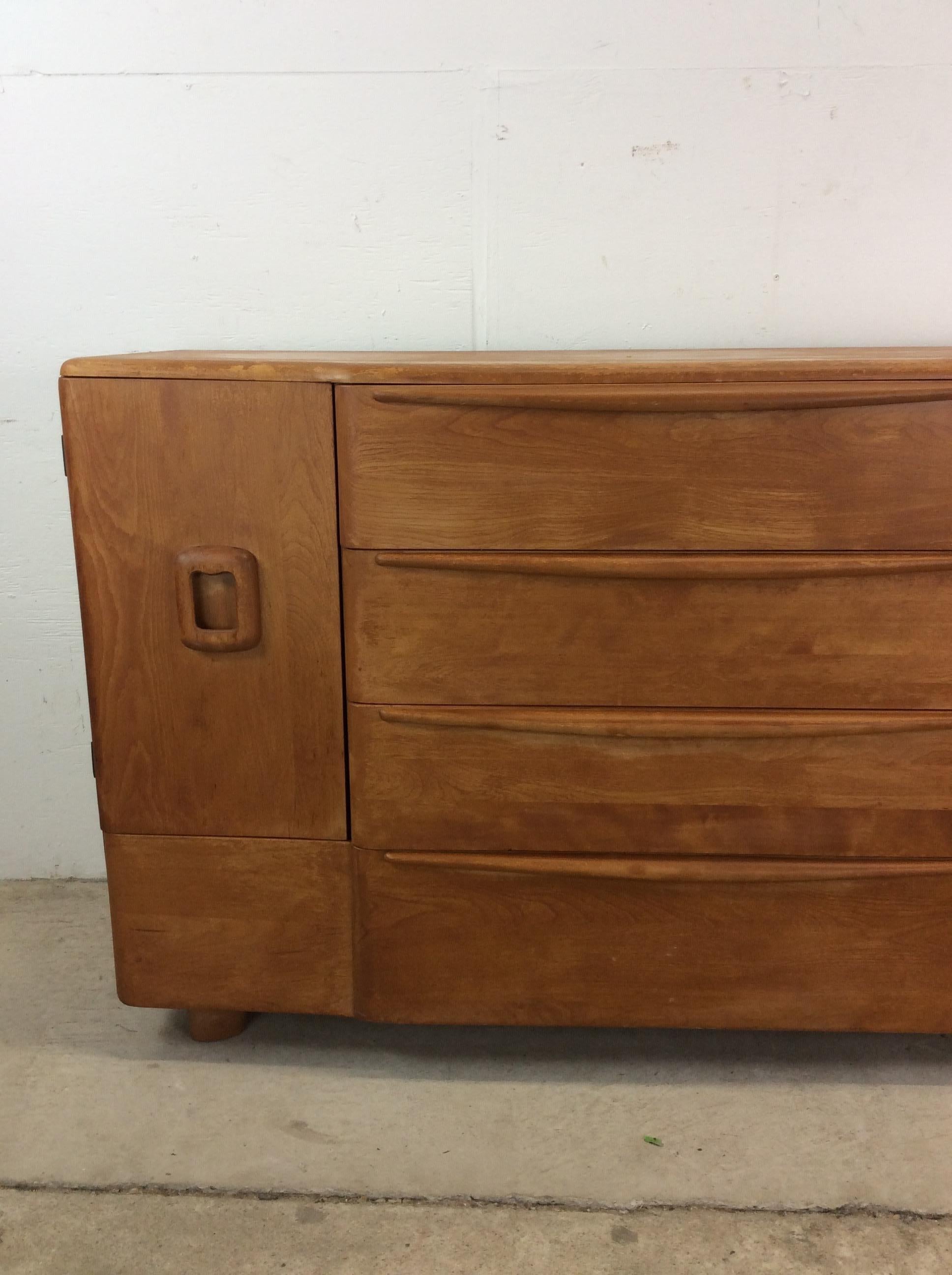 This mid century modern sideboard by Heywood Wakefield features hardwood construction, original champagne finish, four dovetail drawers with wood pulls, and two cabinets with adjustable shelving.  Matching compact credenza, compact China cabinet,