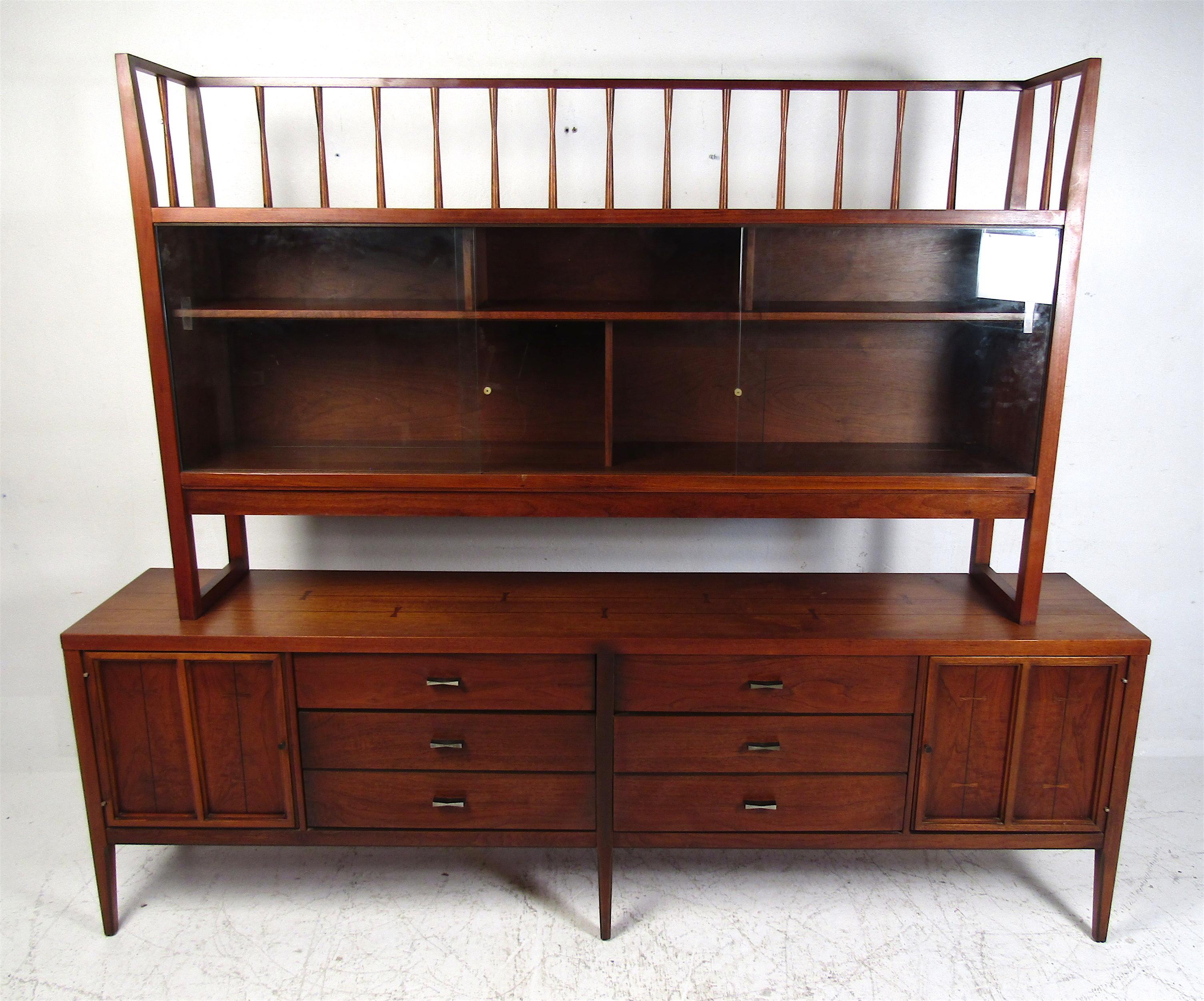 This stunning vintage modern case piece boasts a topper with glass sliding doors and a credenza with tons of storage space. The dark walnut finish with bowtie inlays shows quality craftsmanship. Unusual drawer pulls and sculpted legs add to the