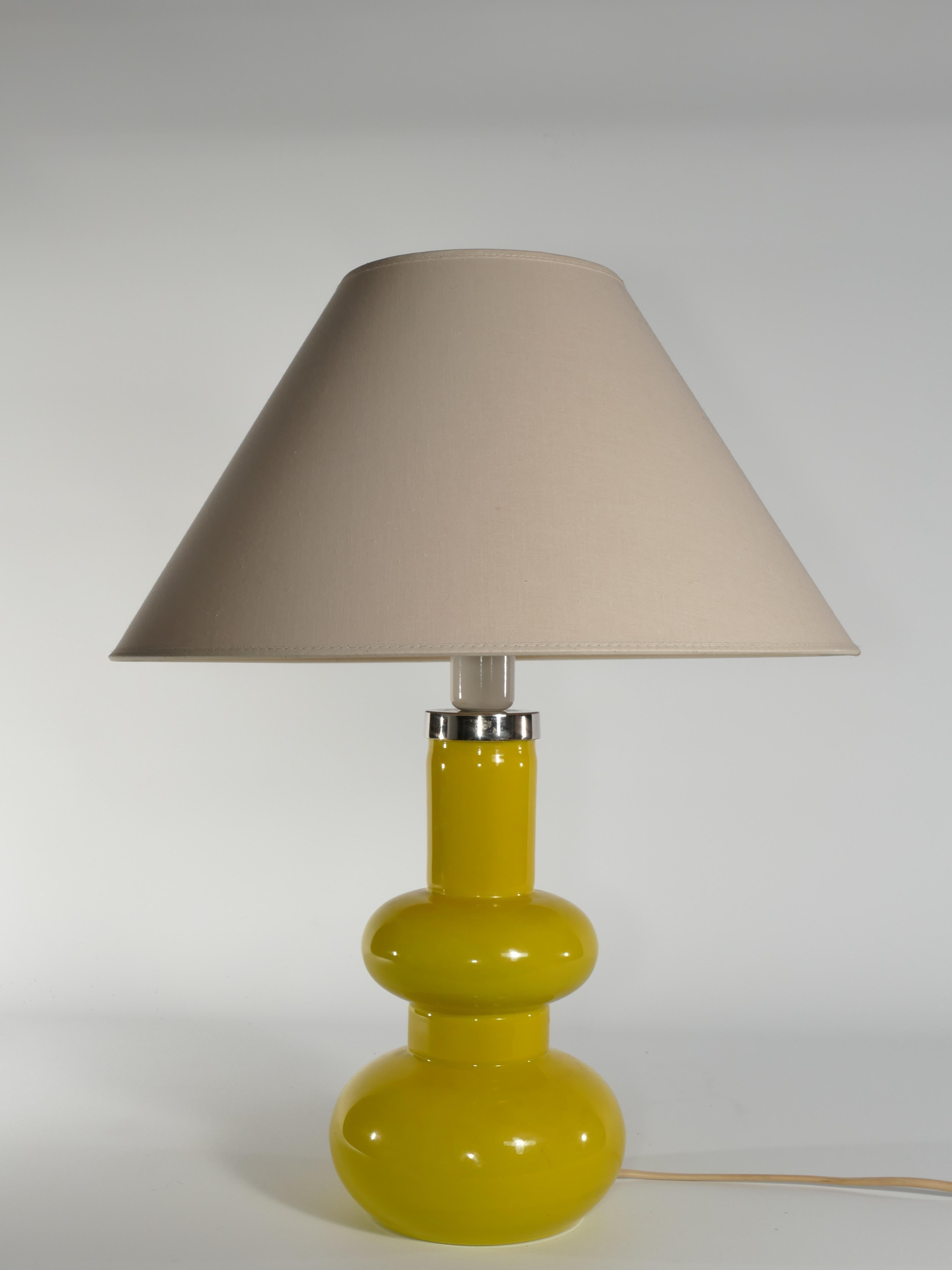 Curvaceous and vibrant, this Mid-Century Modern table lamp by Orrefors boasts a stunning bright yellow hue. The metallic section below the lamp fixture features an engraved 