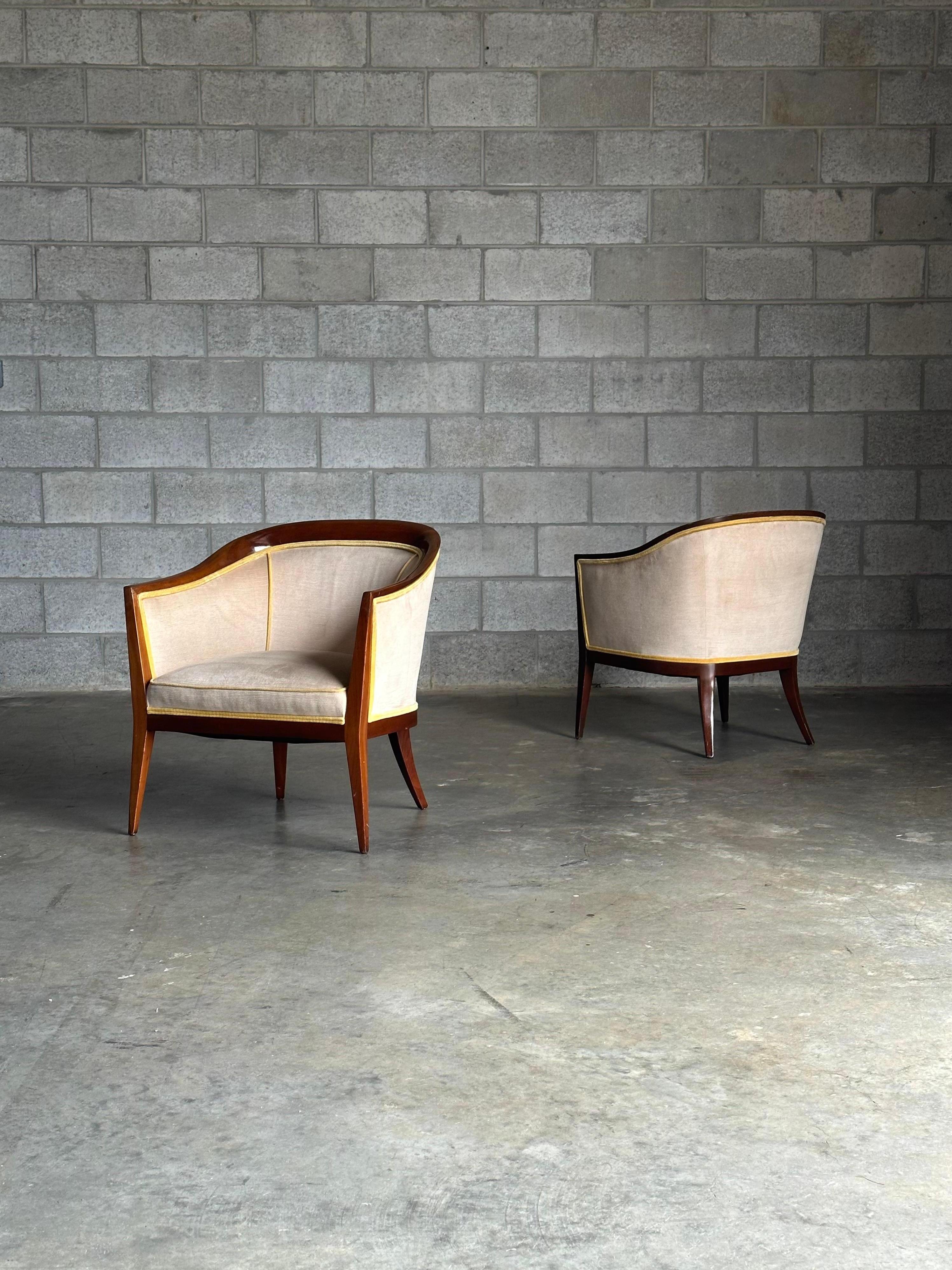 An elegant pair of mid century modern chairs with wonderful sculpted lines. Chairs feature barrel backs accentuated with walnut detail running along the top and continuing into the arms and legs. The chairs were redone at some point in a soft light