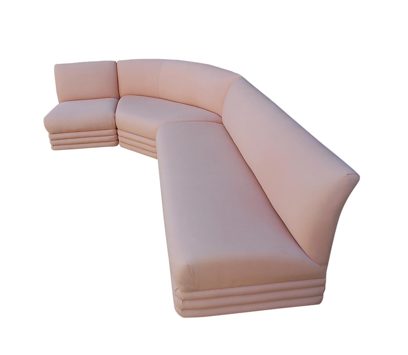 A long curved sectional sofa in original blush pink linen. It features 3 separate sections in Art Deco form.