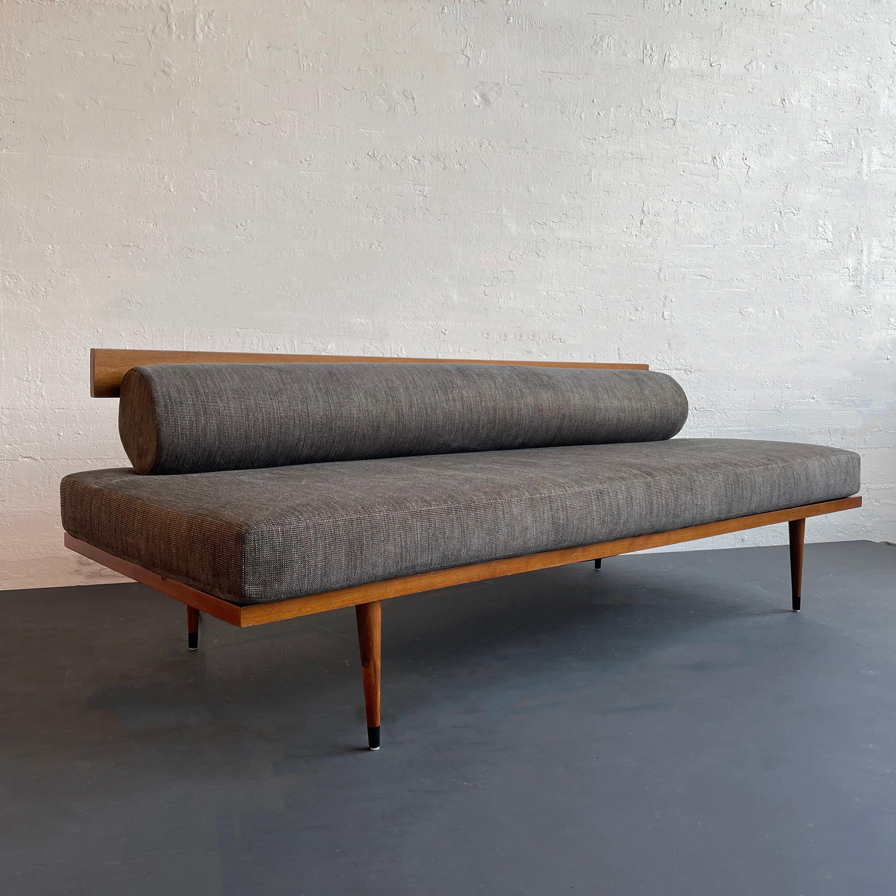 Mid-century modern, sleek, low, maple frame daybed sofa features streamlined, charcoal grey upholstery with rolled back cushion. The minimalist gorgeous frame showcases a sculptural back rest and tapered legs. This design combines functionality with