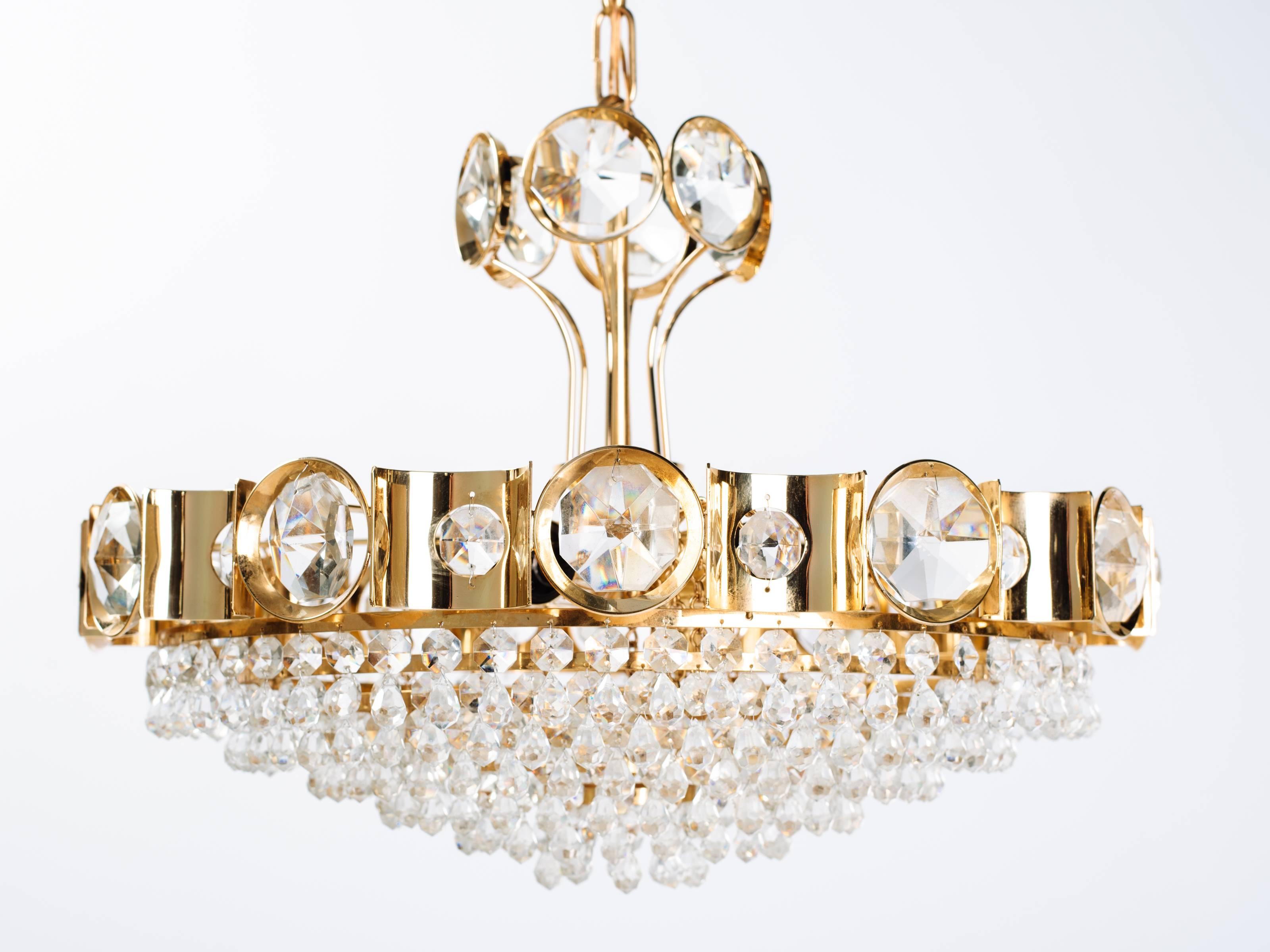 Hollywood Regency gold plated chandelier fitted with tiers of elegant cut crystal pendants and faceted crystal beads. The chandelier has a multi-tier design with a scalloped frame fitted with stunning oversized jeweled crystals along the top.