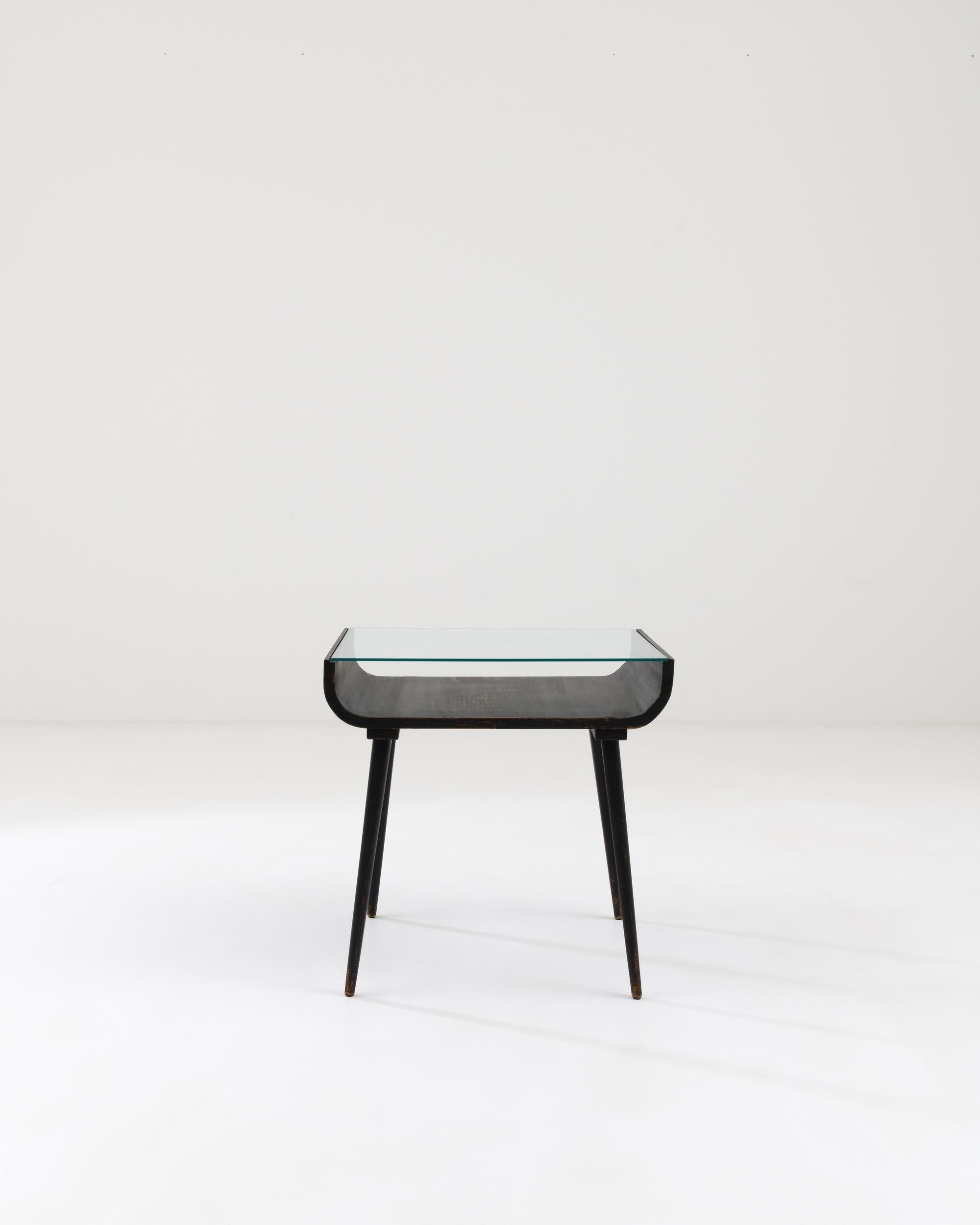 A wooden side table with a glass top made in mid-20th century Czechia. Typical of mid-century Central European design, this side table combines a forthright utility with a minimal sleekness. The wood structure, which has begun to patina throughout