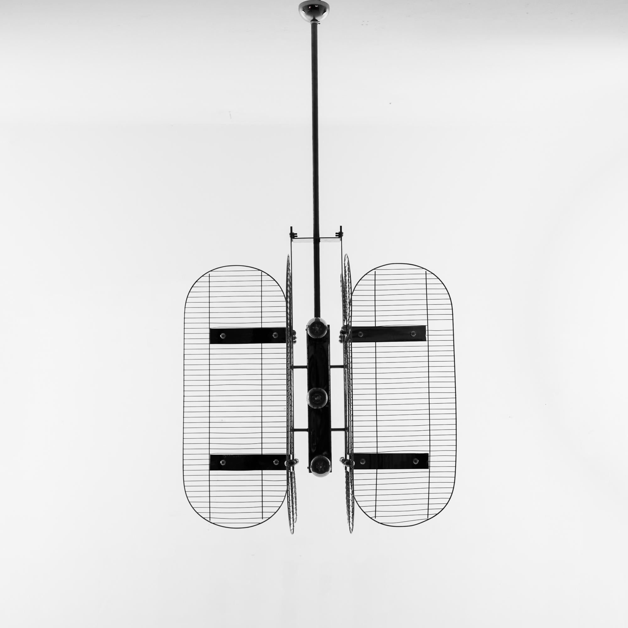 A metal chandelier from Czechia, produced circa 1960. This Mid-Century style pendant features of six lights, flanked by six metal grilles, mounted on a central stalk hanging from the ceiling. The unique geometric design is rendered in stark black