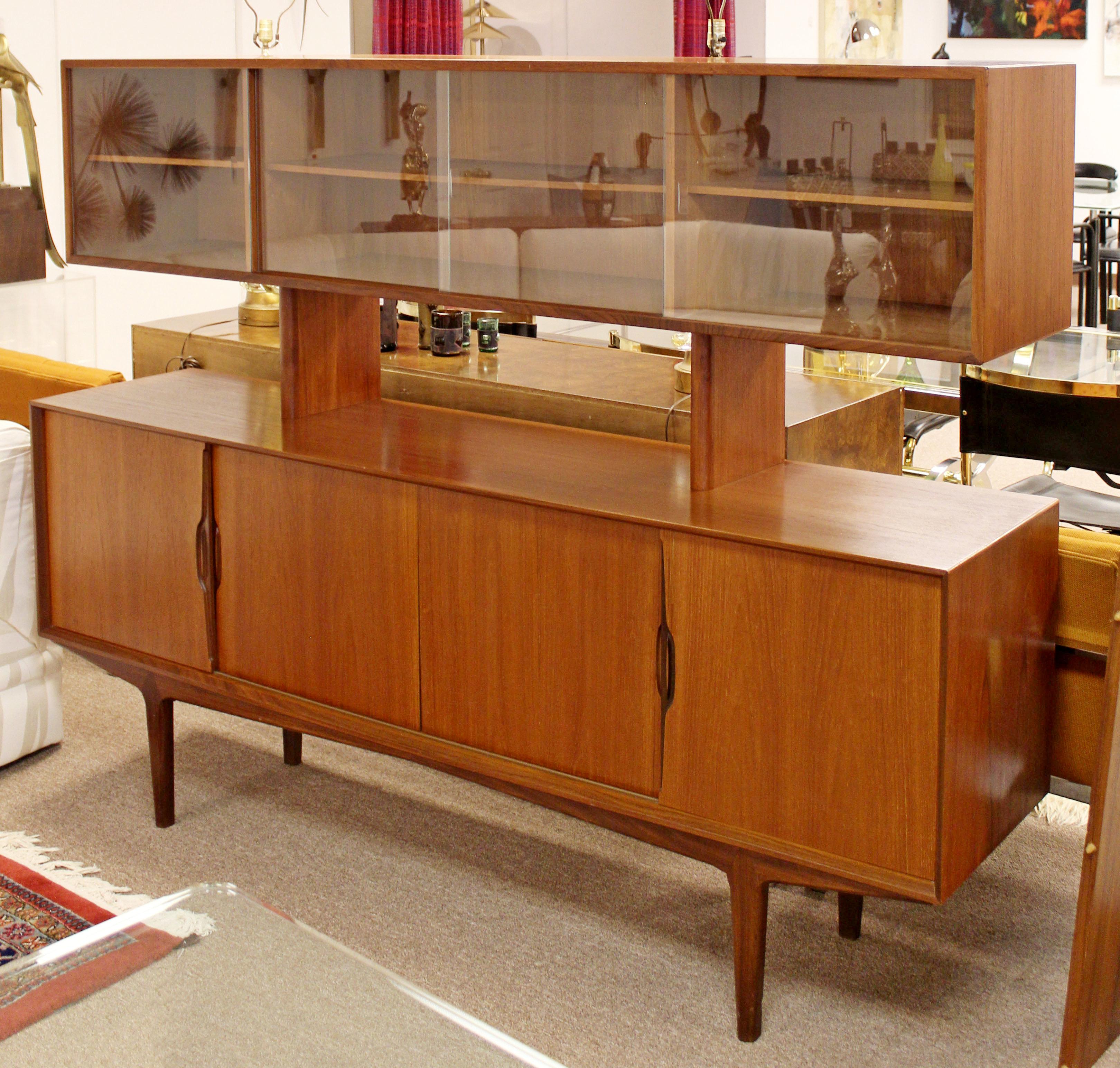 For your consideration is an incredible, two-tiered sideboard, which features lower storage with a series of drawers and doors and a detachable upper shelving component with sliding glass doors, in the style of Kurt Ostervig. In excellent condition.