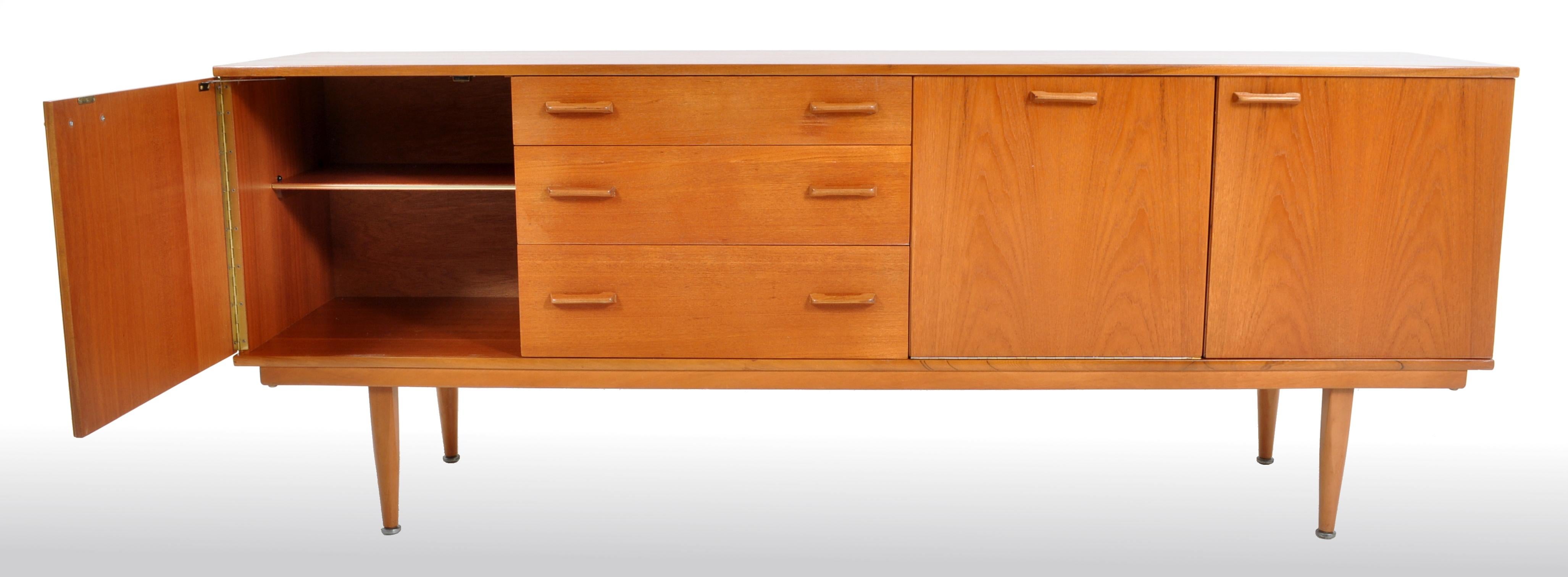 Mid-Century Modern Danish credenza in teak, 1960s. The credenza having a single cupboard door to either end enclosing single shelves. To the center a bank of three graduated drawers next to a fall-front cupboard enclosing a single shelf and mirrored