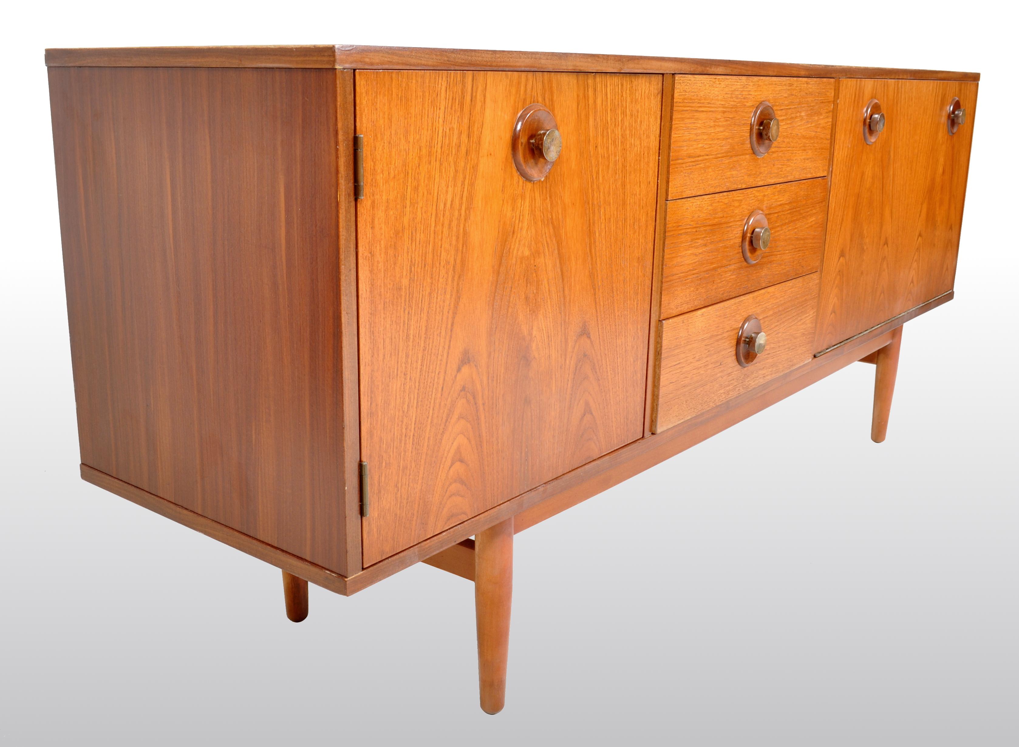 Mid-Century Modern Danish credenza / sideboard in teak, 1960s. The credenza having a cupboard door to the left side with a central bank of three drawers flanked by a large fall-front door enclosing two sections, one with a sliding tray. The credenza