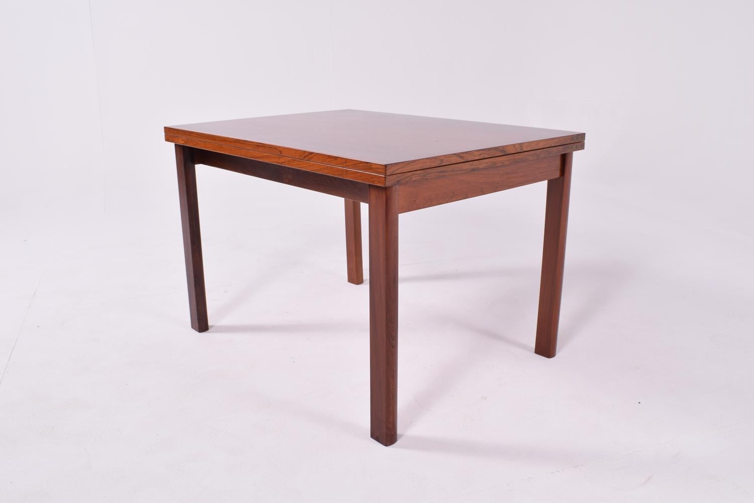 Cette table basse à plateau rabattable est un chef-d'œuvre du design du milieu du siècle, avec un cadre en bois de rose massif qui respire l'élégance naturelle et la durabilité. Le plateau de la table présente des placages de bois de rose