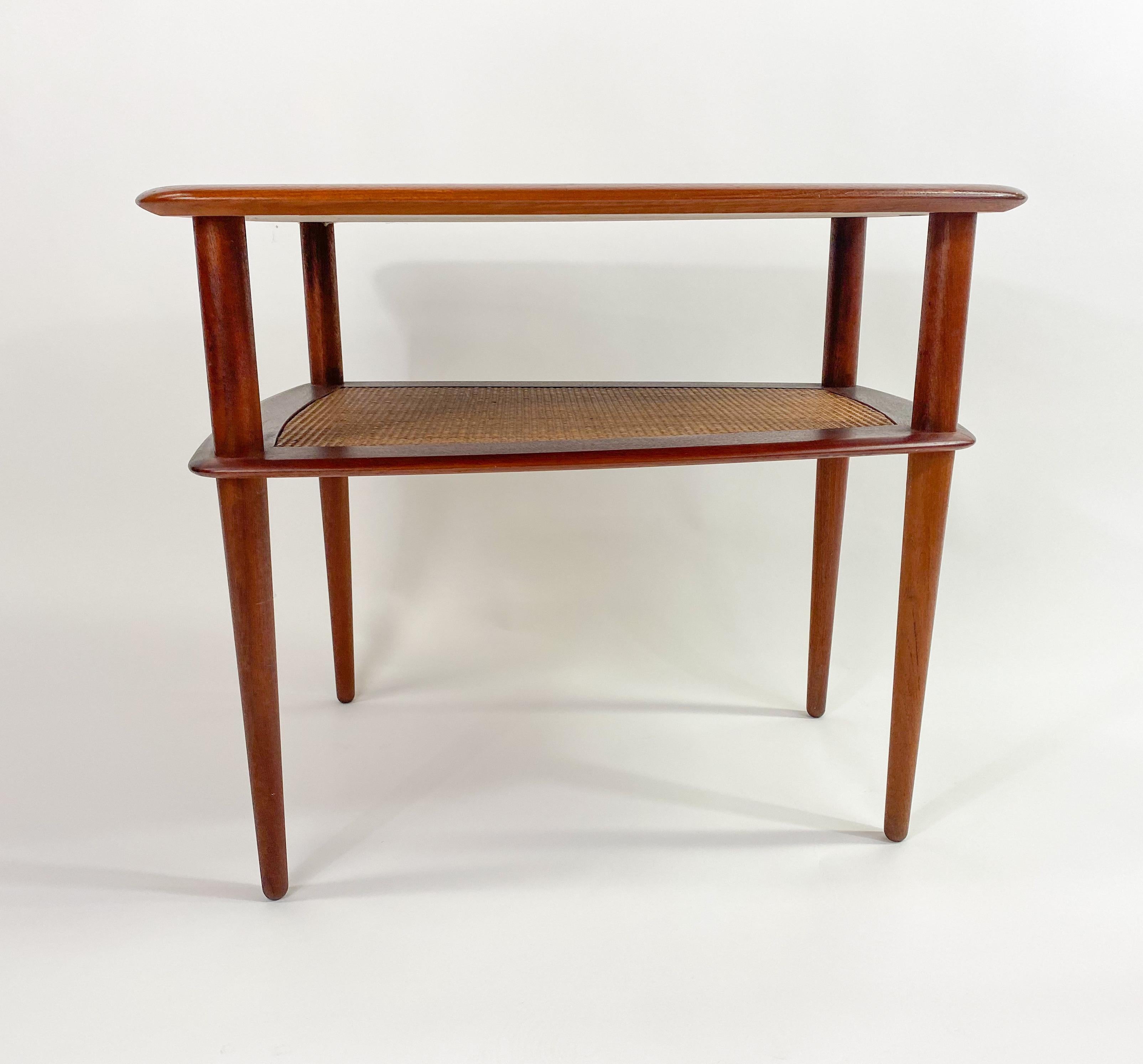 An elegant pair of Mid- Century Modern two tier solid teak side or end tables designed by Hvidt and Molgraad for John Stuart. The tables are marked made in Denmark and have John Stuart stay in the bottom. The high quality tables feature a caned