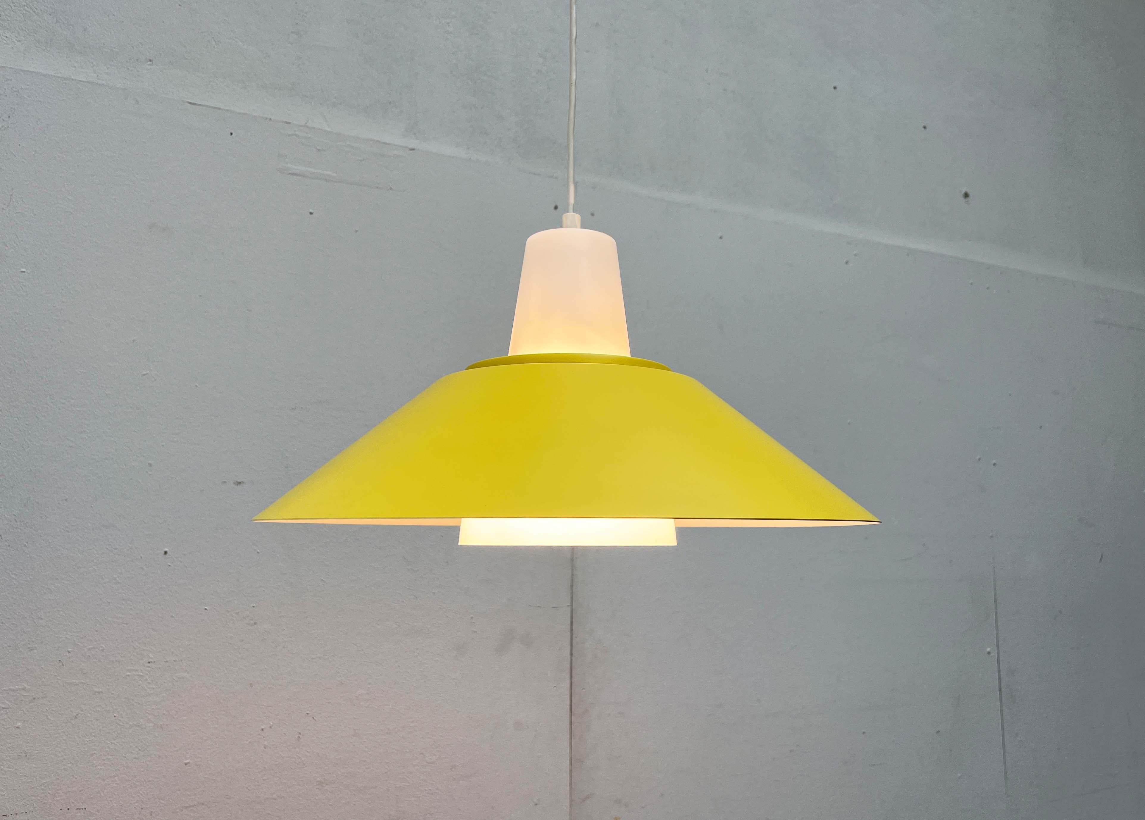 Lampada a sospensione danese degli anni '60.

Un design minimalista con un accento colorato. Il grande paralume è realizzato in metallo e rifinito in giallo sulla parte superiore. La cupola della lampada è realizzata in plastica traslucida. Un cono