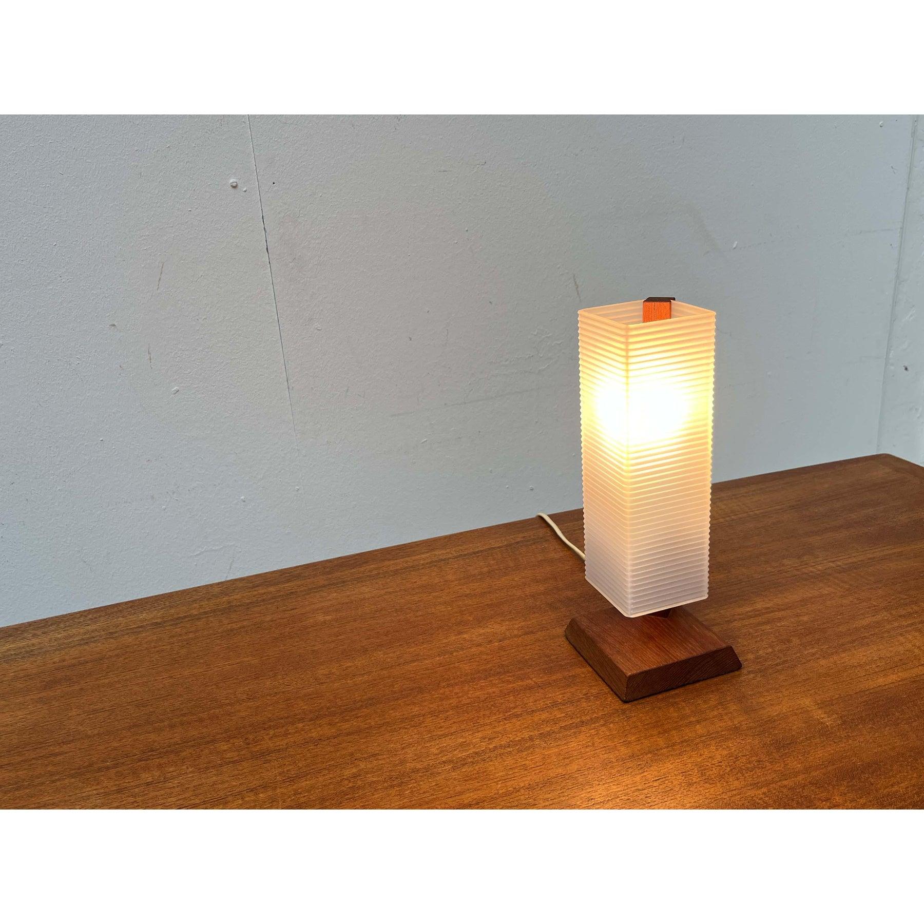 Lámpara de sobremesa de mediados de siglo de dinamarca.
un diseño minimalista. La base de teca tiene una forma básica cuadrada y presenta un bisel alrededor. Un eje de teca sobresale hacia arriba de la esquina trasera. Un difusor rectangular de