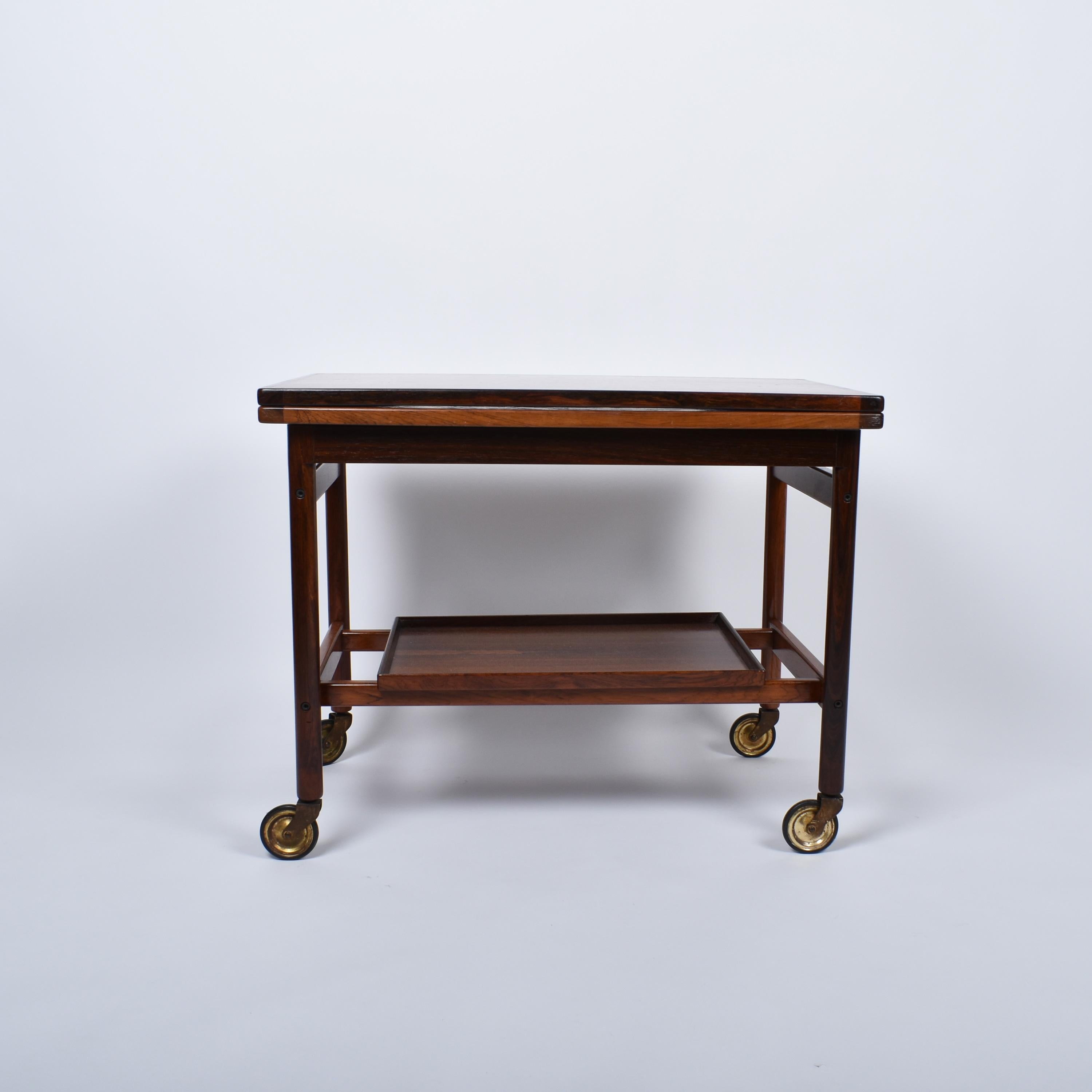 Santos bar cart with removeable tray.
The top slides to unfold and reveal a stain proofed black melamine.
Designed by Kurt Østervig in the sixties. 
One can still admire the master's attention for details, like nice joinery or assemblages, and this