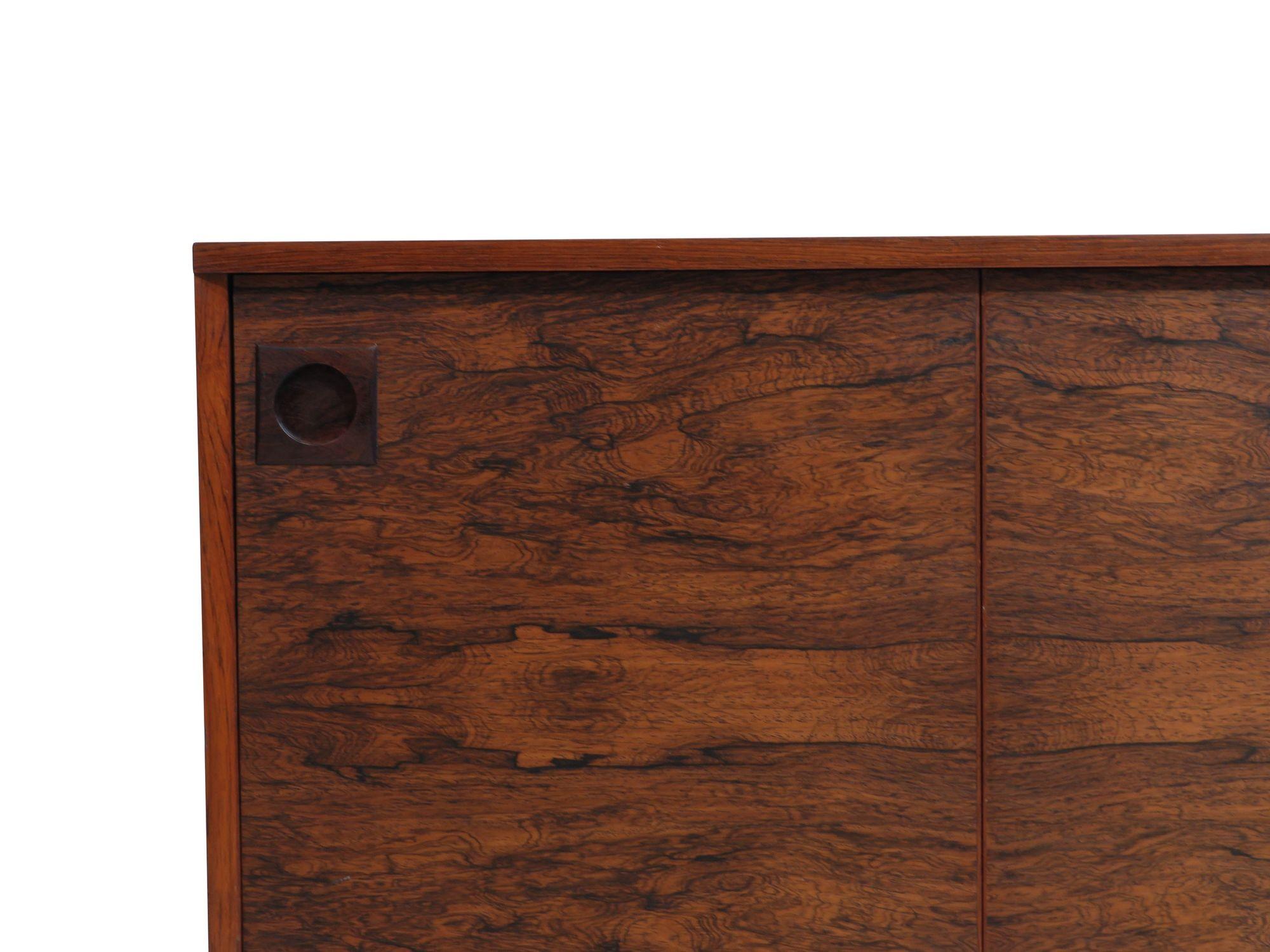 Finely crafted Brazilian rosewood cabinet with dynamic book-matched grain on the doors with unique sliding door mechanism, bullet-shaped brass hinges and sculpted pulls. The interior is finished in rosewood with adjustable shelves and a felt lined