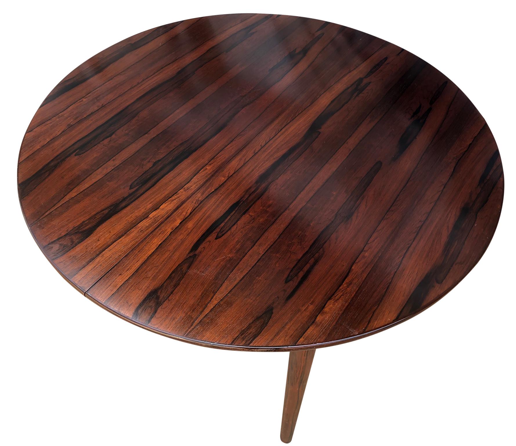 Midcentury rosewood expandable round dining table with 1 nesting leaf. This is a beautiful dining table Made in Denmark. Amazing solid rosewood legs. Made, circa 1960. Original finish in excellent condition. Documented and stamped under leaf AM