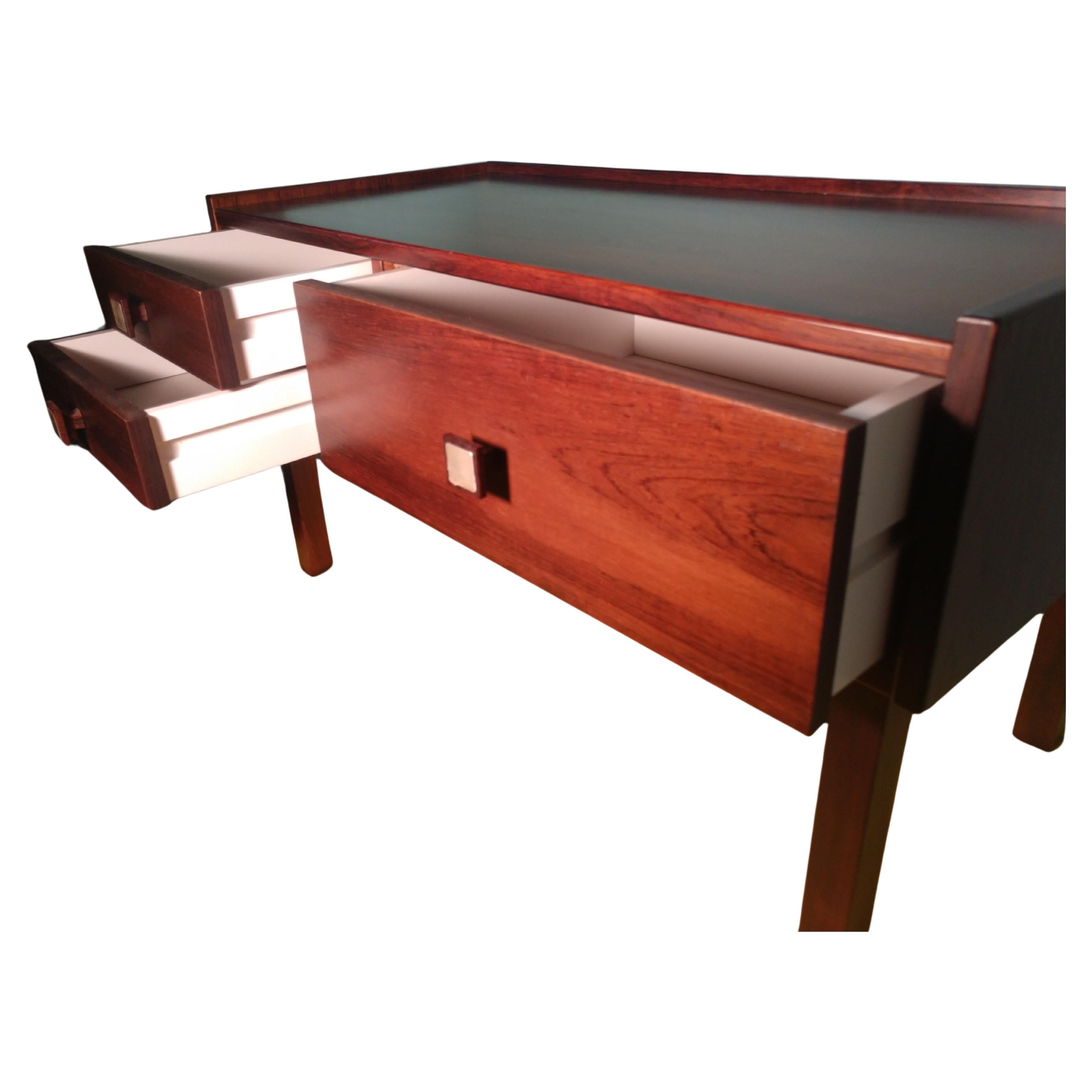 Snello, semplice ed elegante tavolo a 3 cassetti in palissandro.
Due cassetti a sinistra e uno più grande a grandezza naturale a destra.
Molto robusto e compatto, ottimo per uno spazio ristretto. In eccellenti condizioni vintage con un'usura minima 