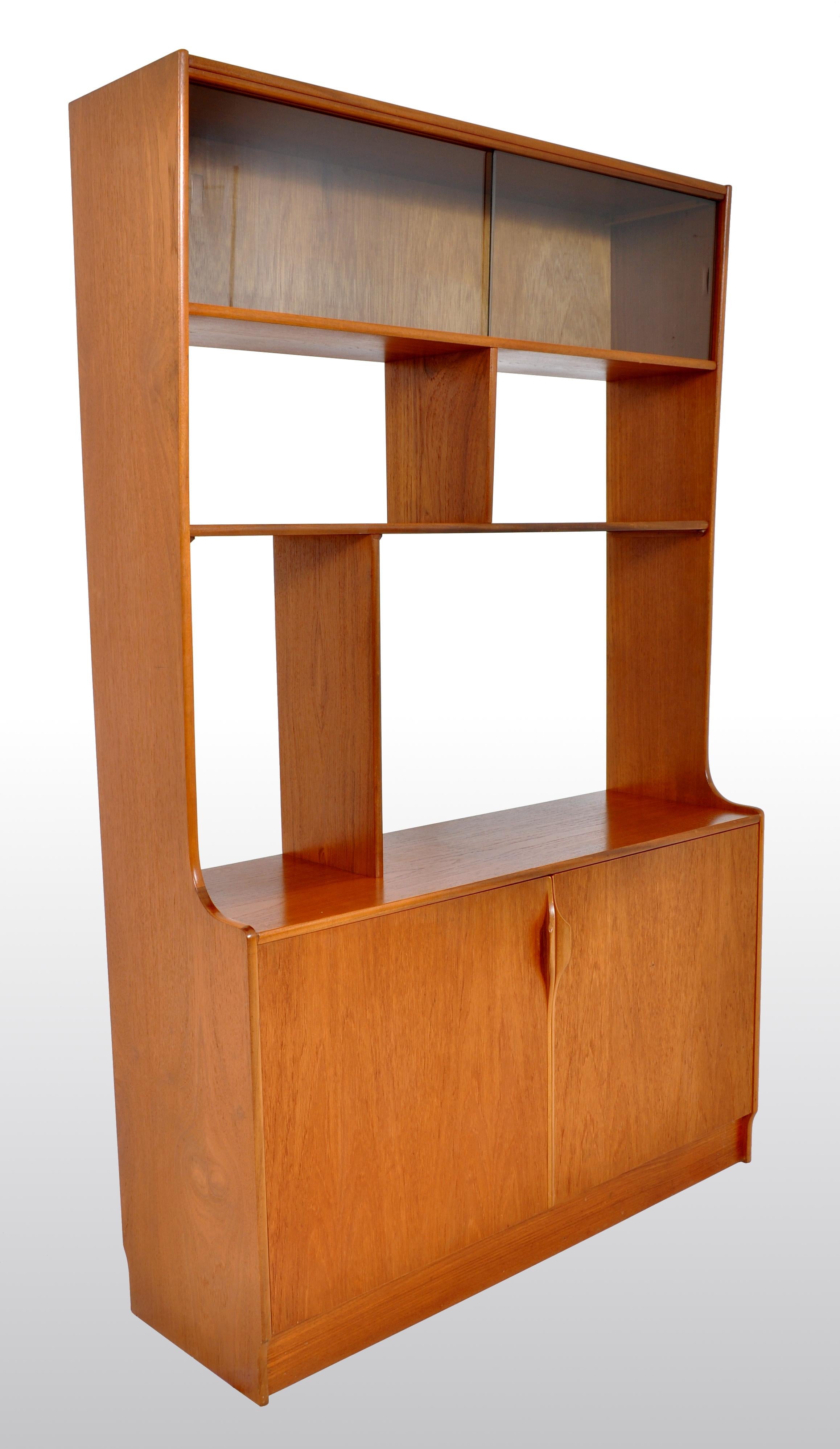 Mid-Century Modern Danish style bookcase / wall unit / in teak by S Form, 1960s. This unusual room divider having an enclosed unit to the top with a pair of sliding glass doors, below are three geometric bookshelves. The sides having an outswept
