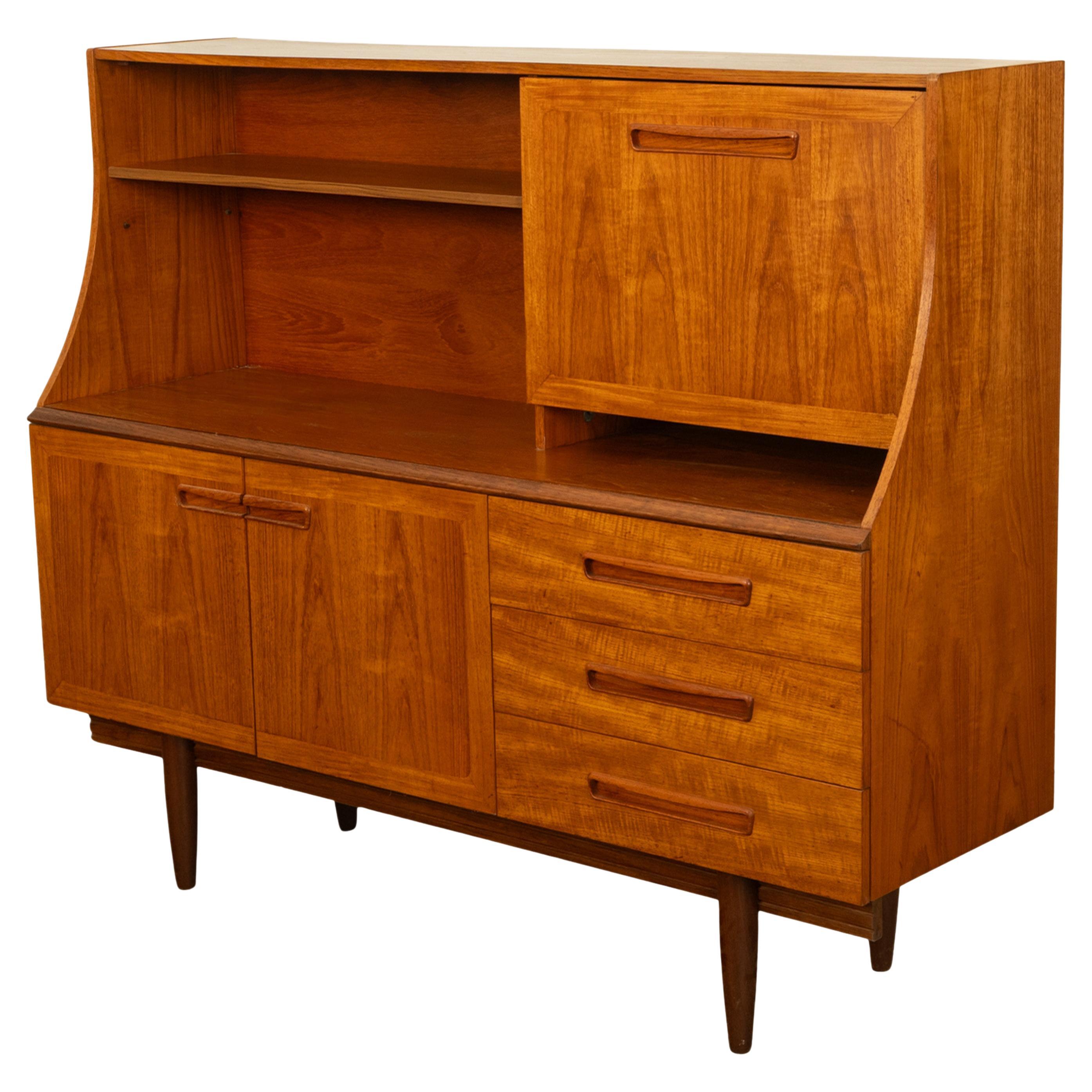Une crédence bar en teck très élégante et originale, de G-Plan, dans les années 1960.
Cette très chic crédence à deux niveaux est fabriquée en très beau teck grainé figuré, avec un plateau aux côtés incurvés et une bibliothèque sur le côté gauche