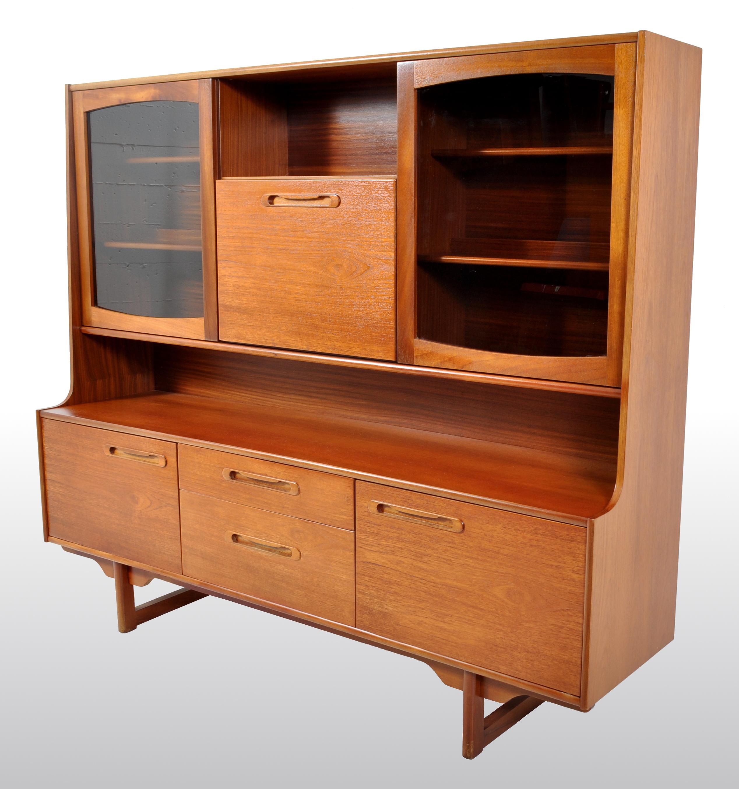 Mid-Century Modern Danish style twin tier credenza in teak by Portwood, 1960s. This unusual twin tier credenza having a central fall-front desk/bar and flanked by twin smoked glass doors, each enclosing two shelves. The base having a pair of twin