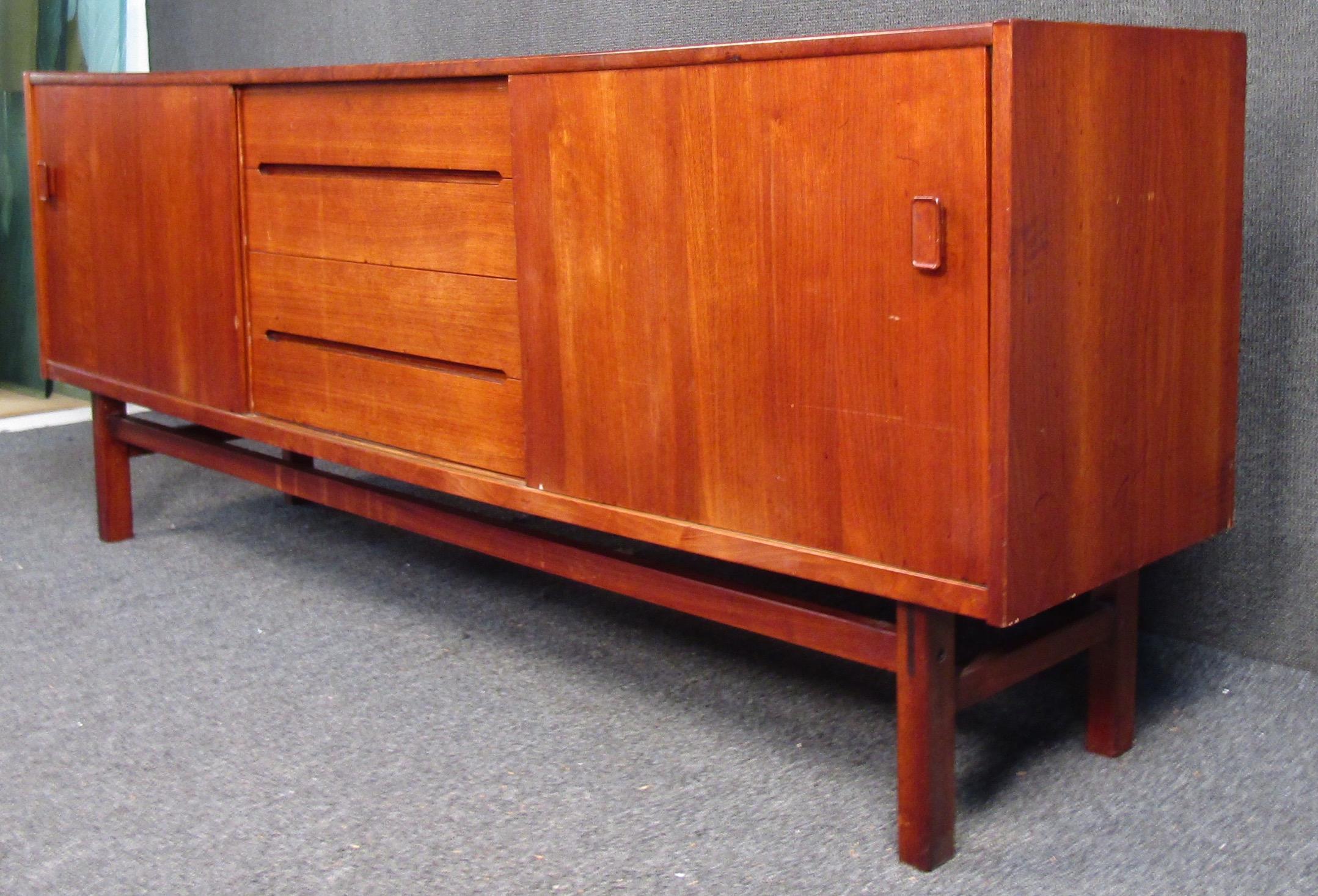 Vintage teak sideboard featuring four drawers and two sliding doors. Elegant Scandinavian Modern sideboard features storage for dining room or use as a mid-century style TV or office console. Stylish teak finish adds vintage Danish flair to any